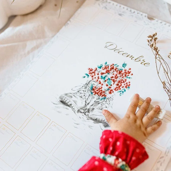 Main d’enfant sur un calendrier de décembre illustré de baies rouges et de feuillage.