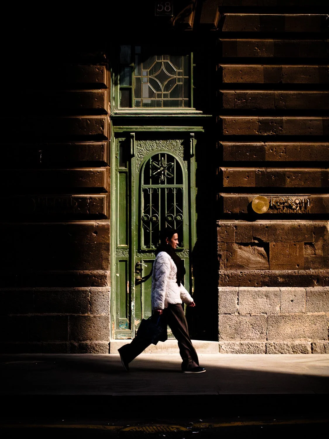 Woman walking past an ornate green doorway set in a historic stone building.