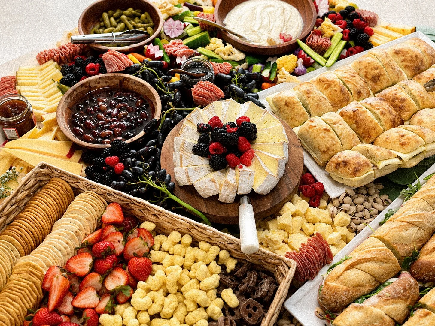 Large charcuterie spread with cheeses, crackers, cured meats, fruit, vegetables, dips, olives, and assorted sandwiches