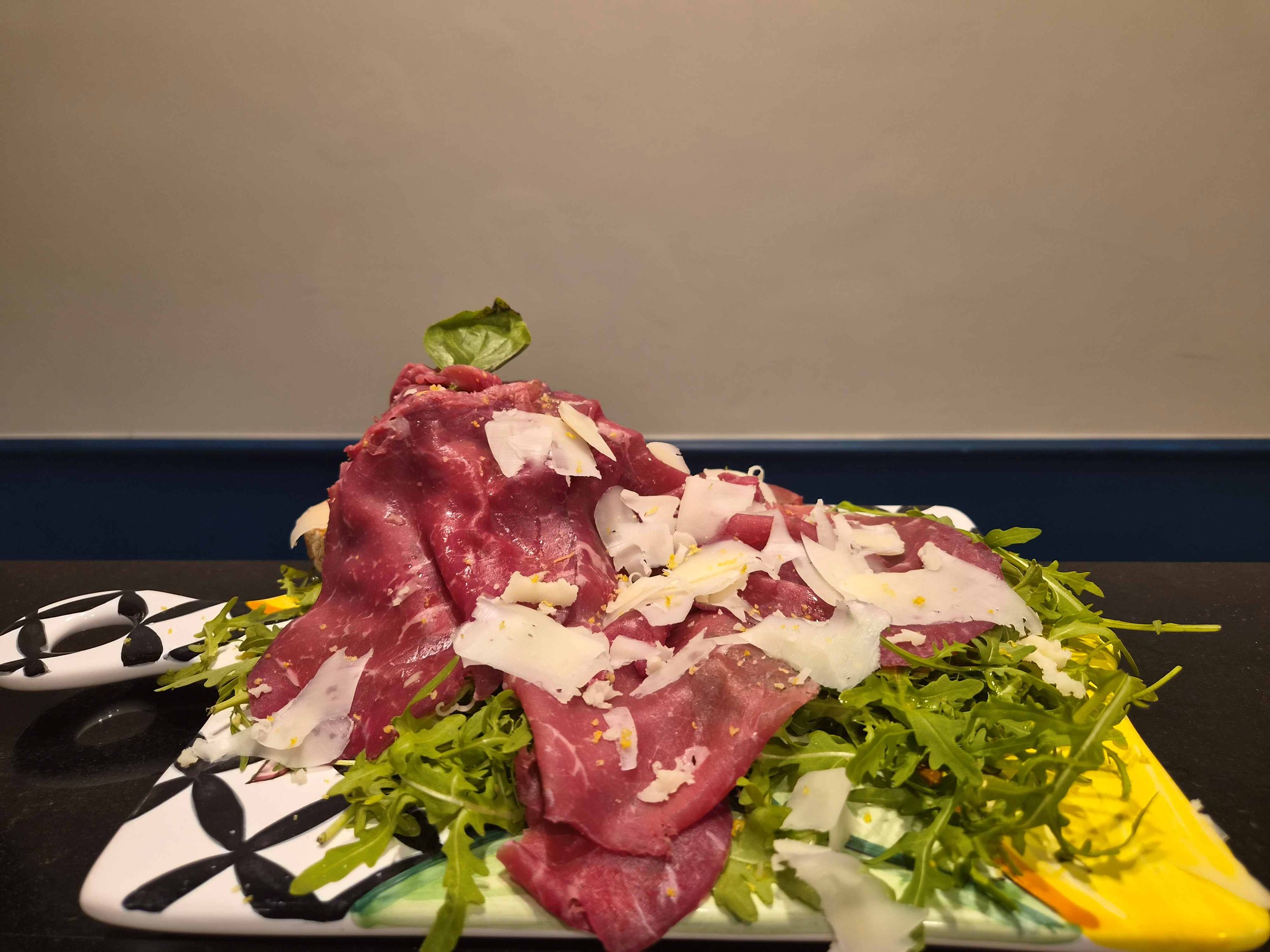 Carpaccio di manzo con rucola, scaglie di Parmigiano, limone e decorazione di basilico su piatto da portata.