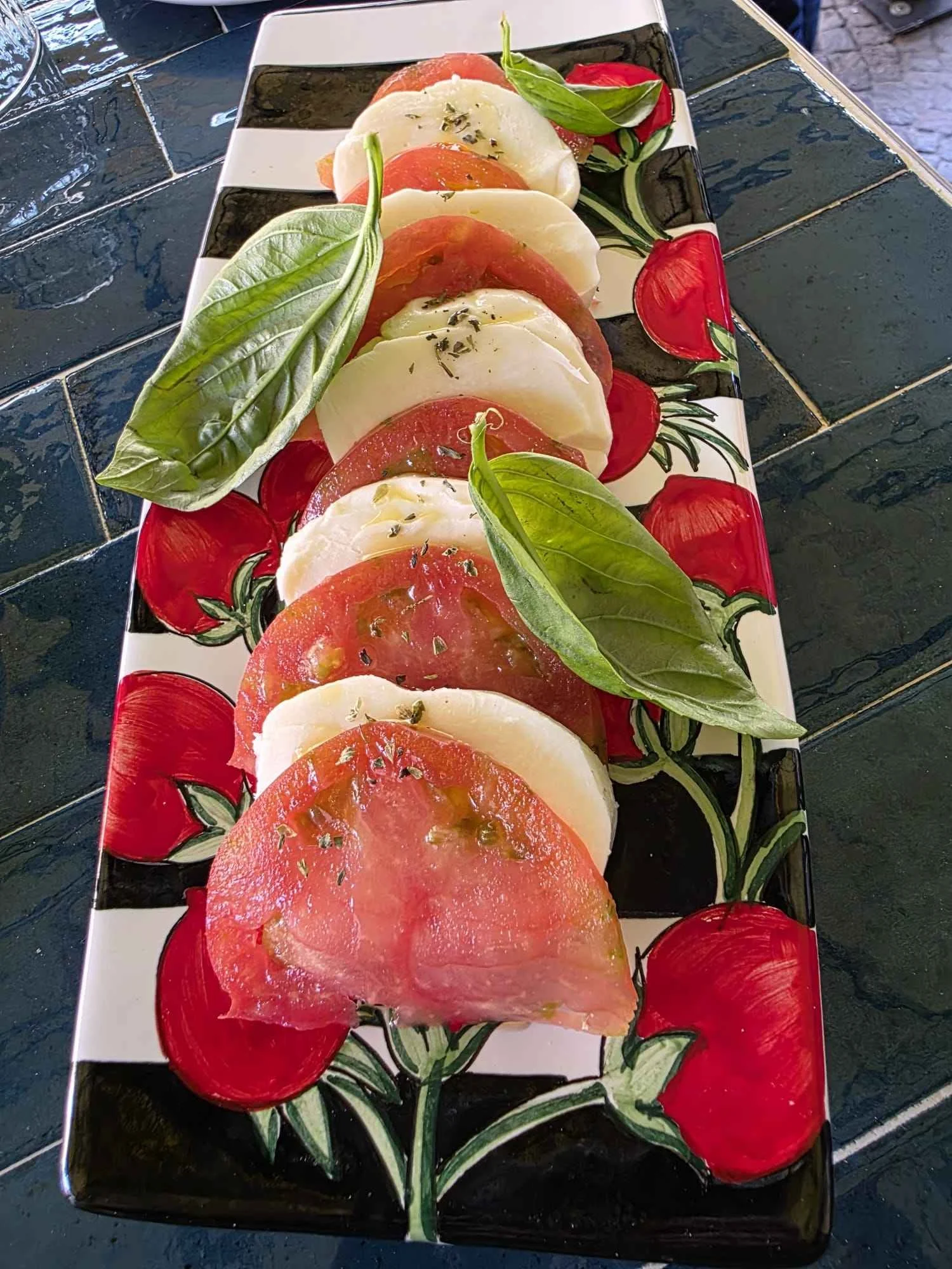 Insalata caprese con fette di pomodoro, mozzarella, basilico fresco, olio d'oliva e origano su un piatto decorato