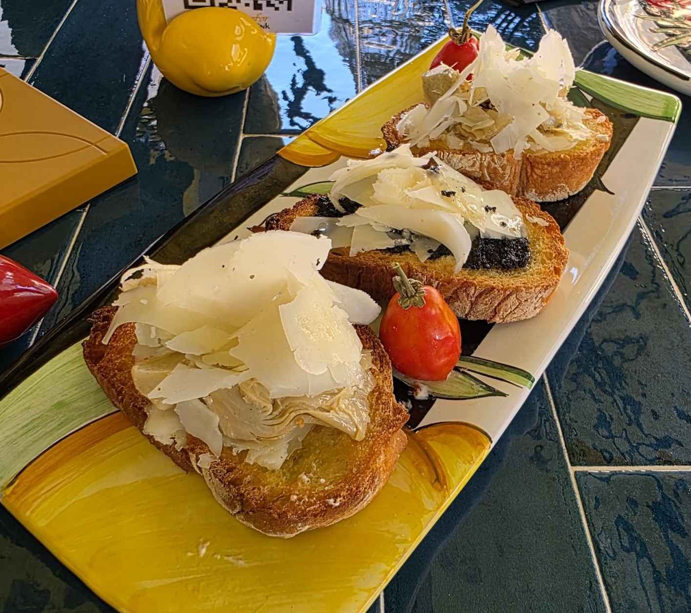 Tre bruschette con crema, scaglie di formaggio e pomodorini su un piatto colorato