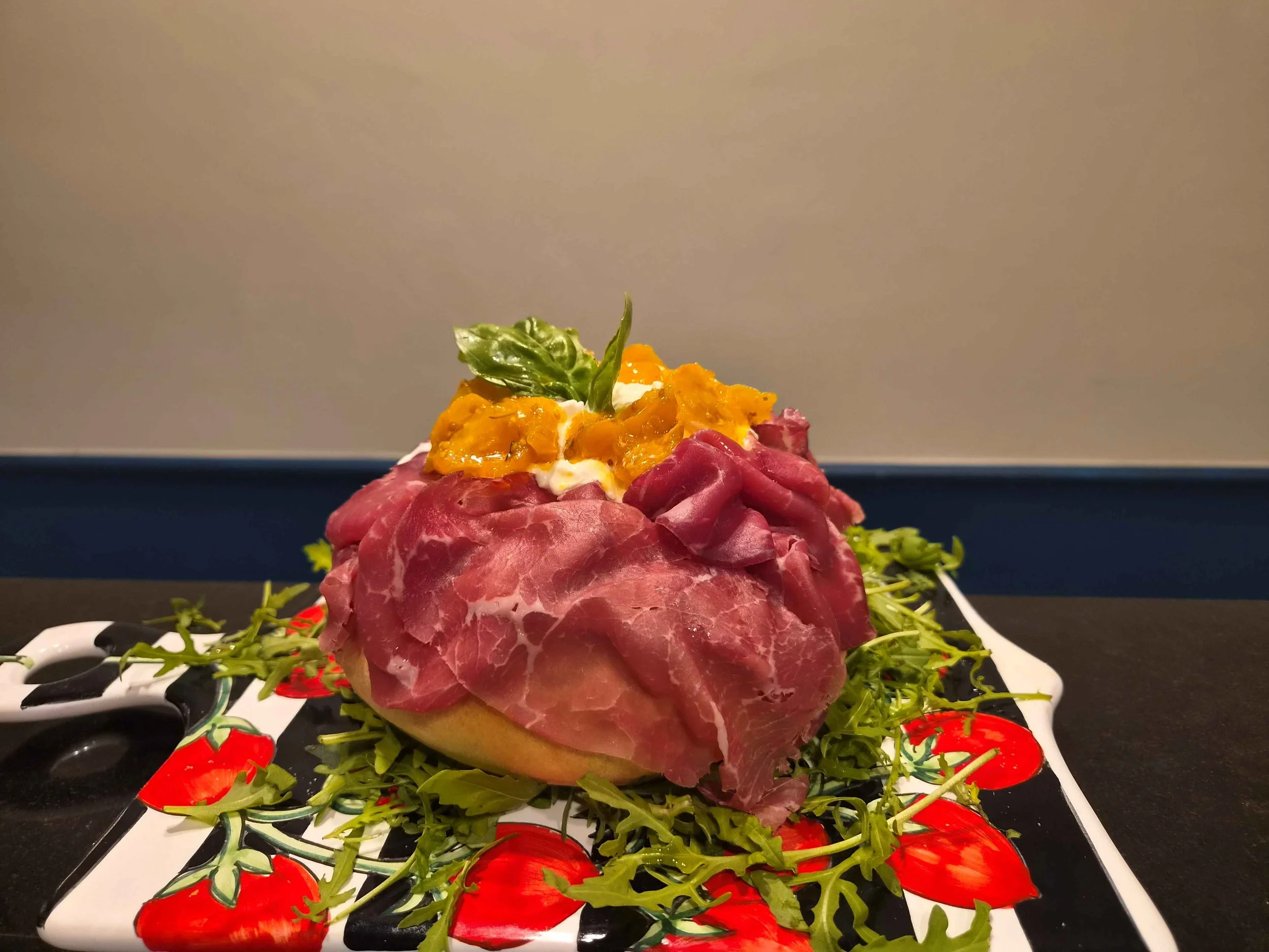 Piatto gourmet con carpaccio di manzo, burrata, pomodorini gialli, rucola e basilico, guarnito con pomodori rossi.