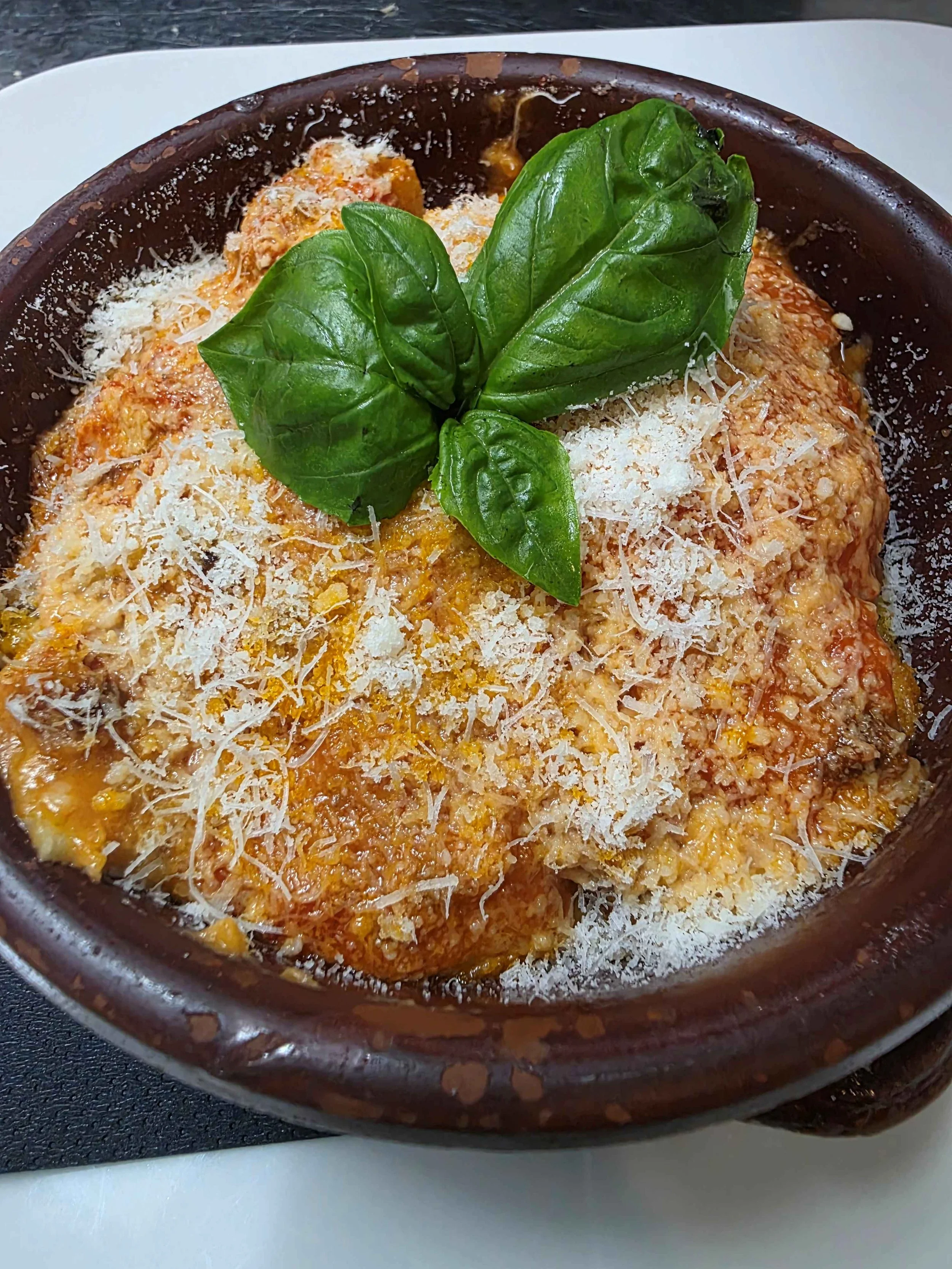 Piatto di pasta al forno con salsa di pomodoro, formaggio grattugiato e foglie di basilico fresco.