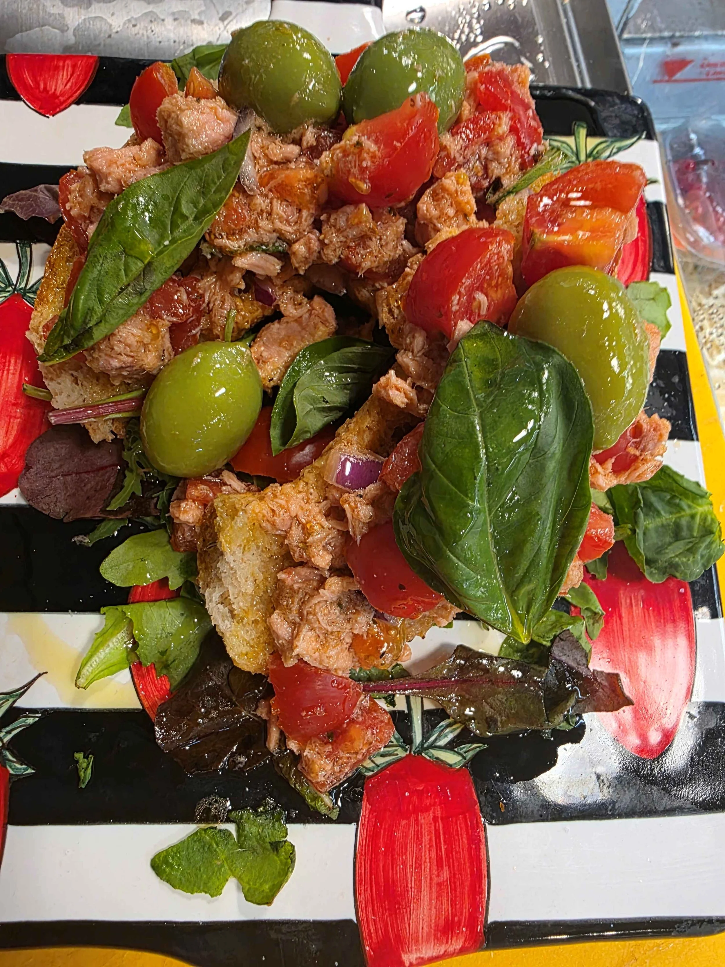 Caponata  con pomodori, olive, tonno e foglie di insalata, guarnito con erbe fresche.