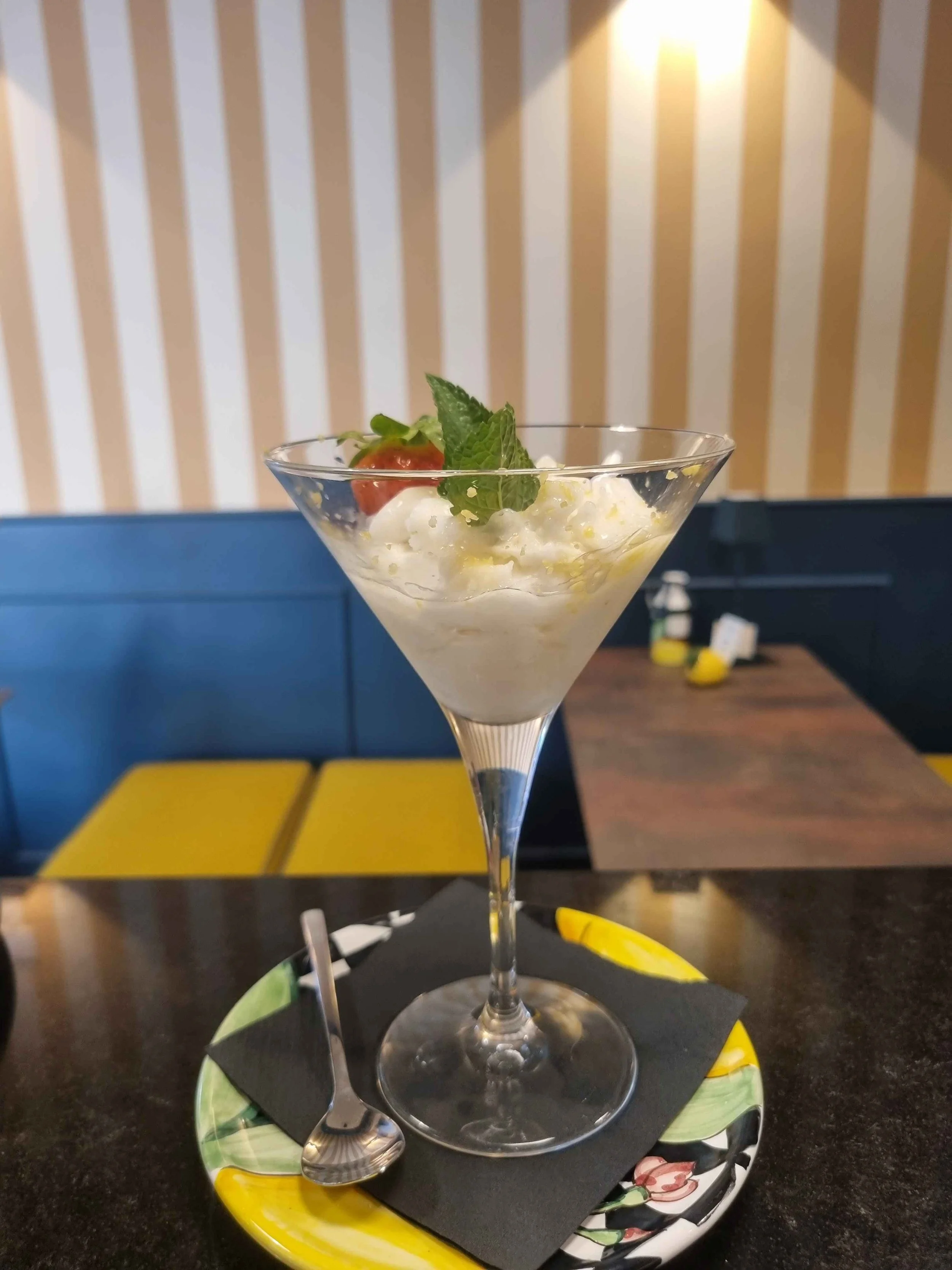 Cocktail analcolico ghiacciato in una coppa da martini, guarnito con menta e fragola su un tavolo da ristorante.