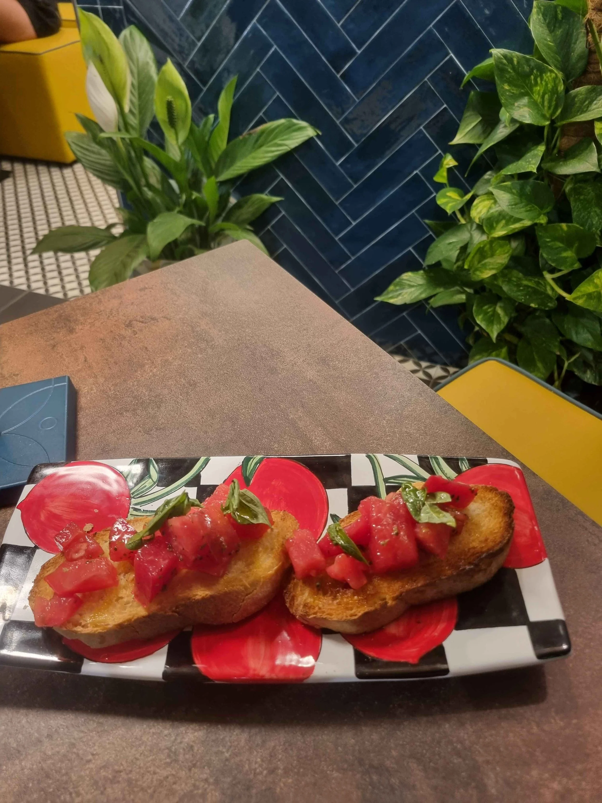 Bruschette croccanti con pomodori freschi e basilico su un piatto decorato, circondate da piante verdi.