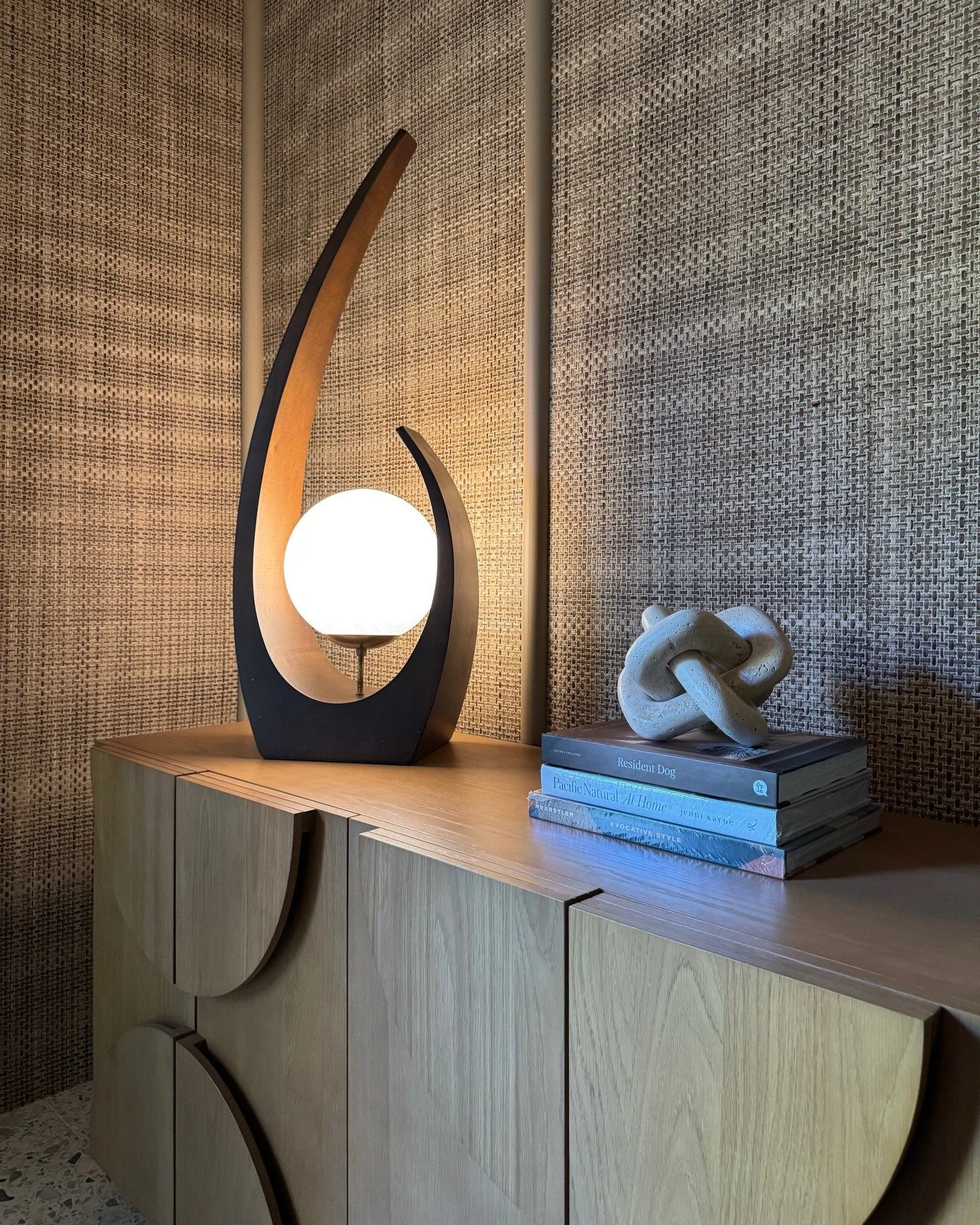 Sculptural wood lamp and books on a curved cabinet