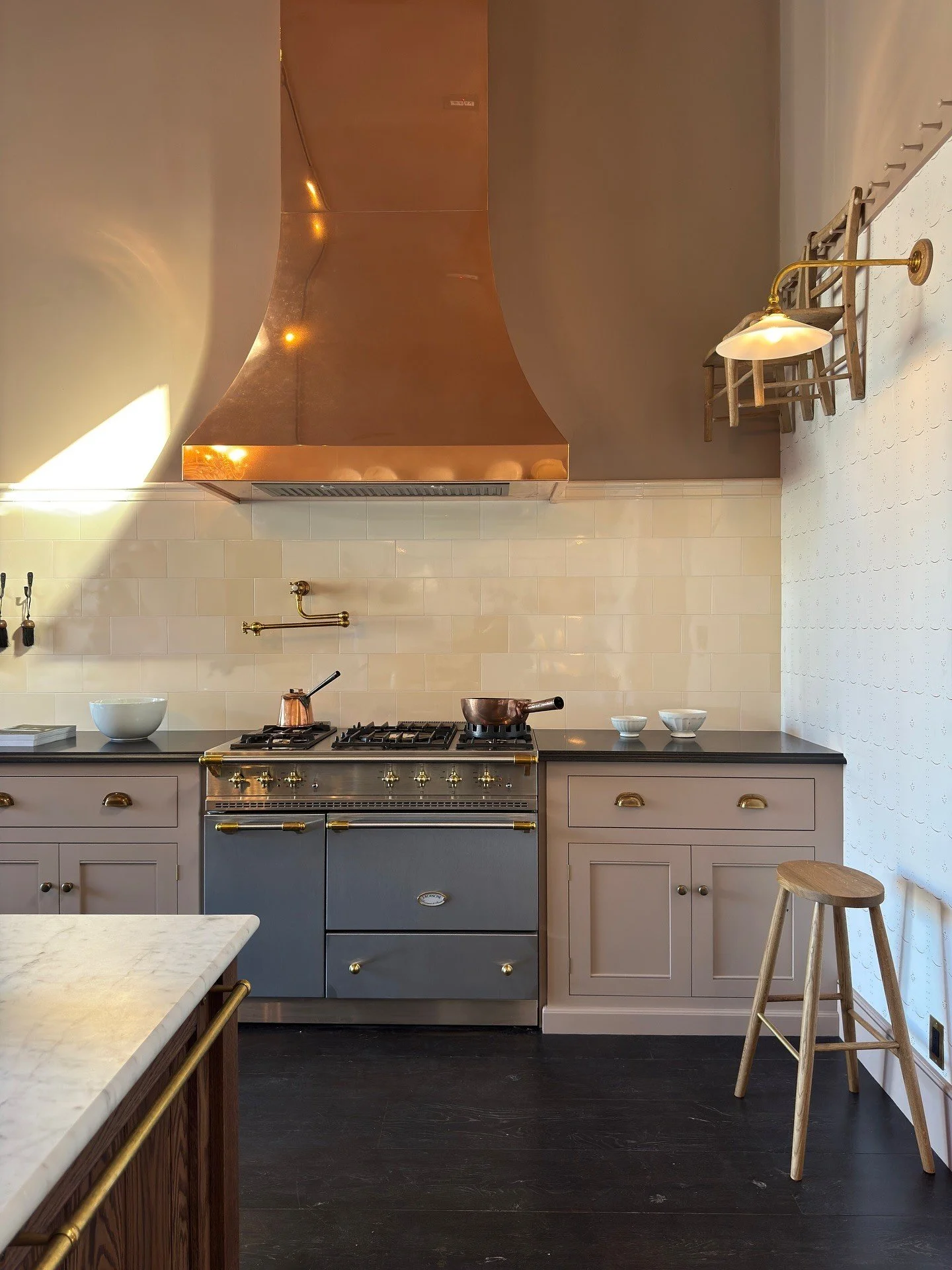 Copper hood above a pale kitchen and a dark range