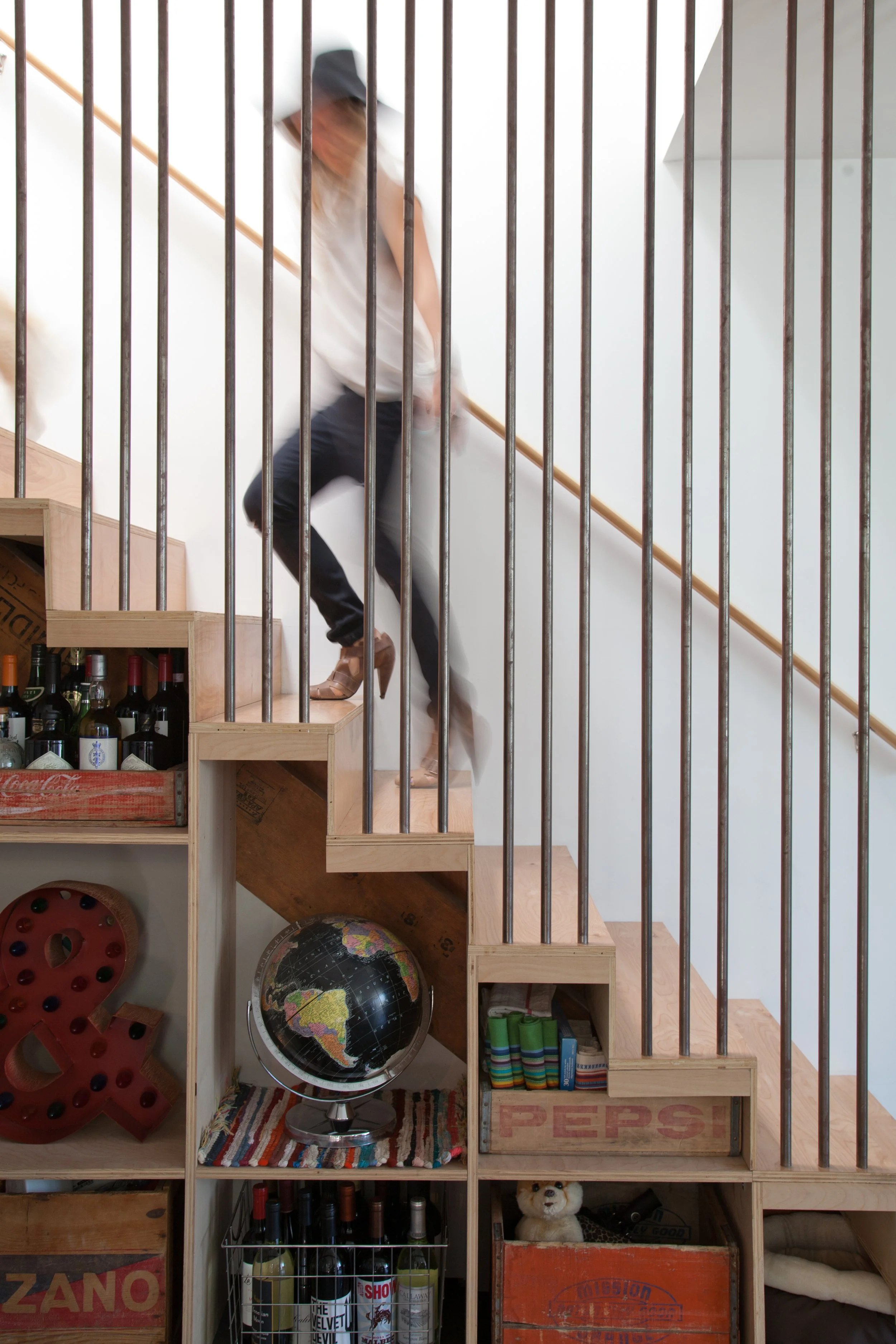 Person on a wood staircase beside a built-in bookcase and vertical railing.