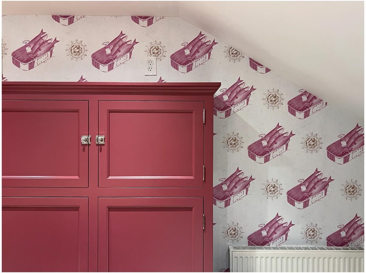 Burgundy cupboard doors beneath illustrated wallpaper and a sloping ceiling