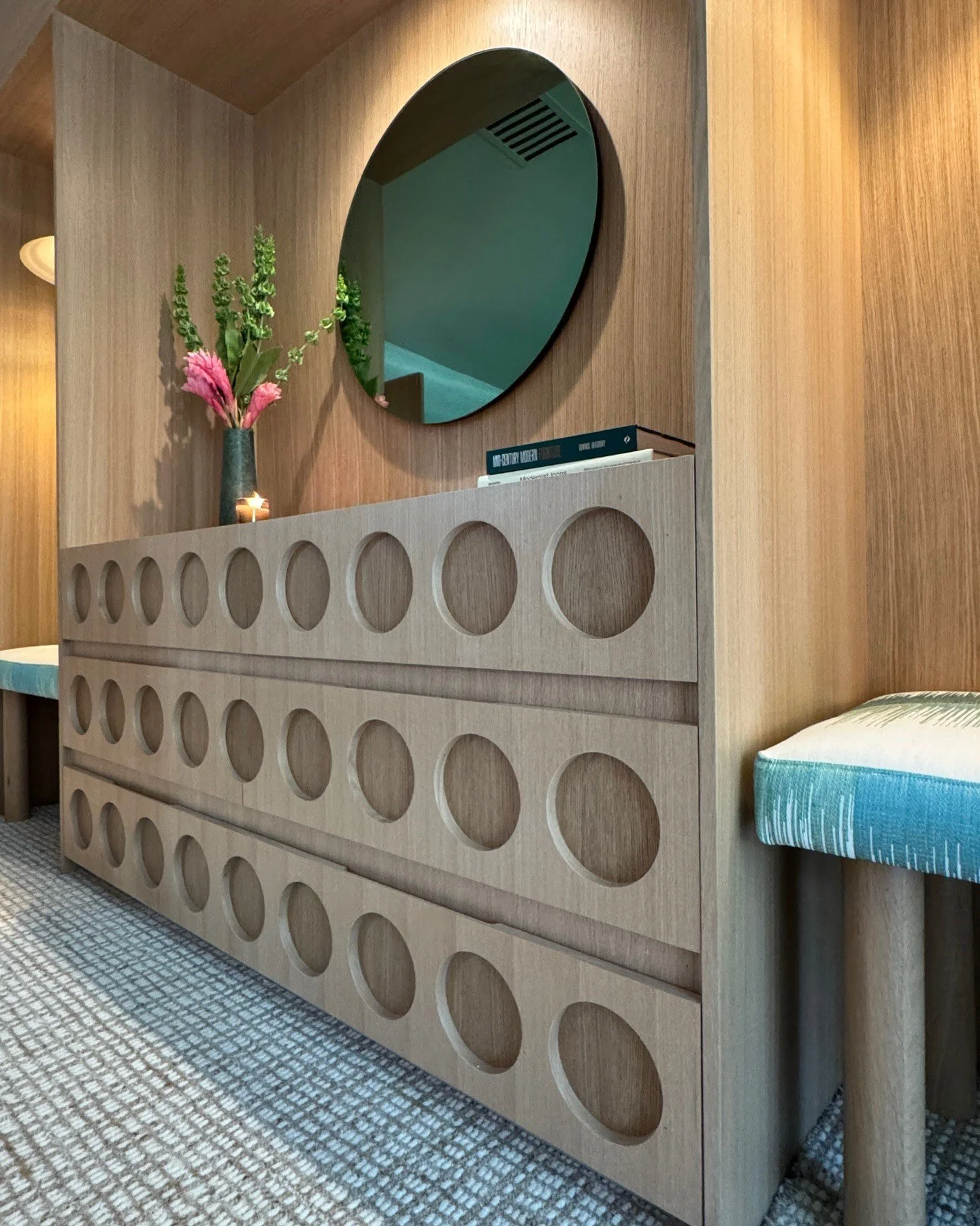 Wood sideboard with circular detailing and a green round mirror