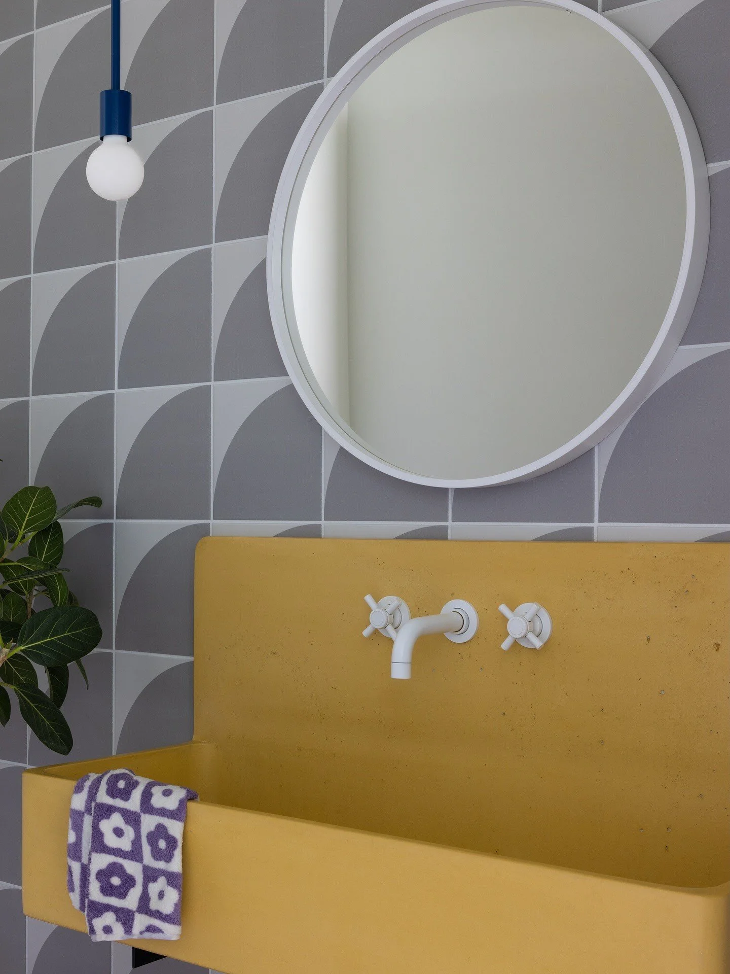 Yellow trough sink beneath gray geometric tile and a round mirror