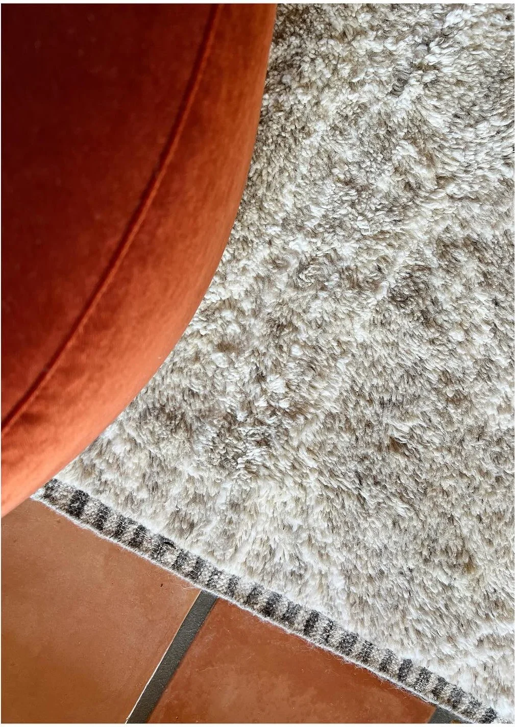 Detail of a pale woven rug beside an orange upholstered chair