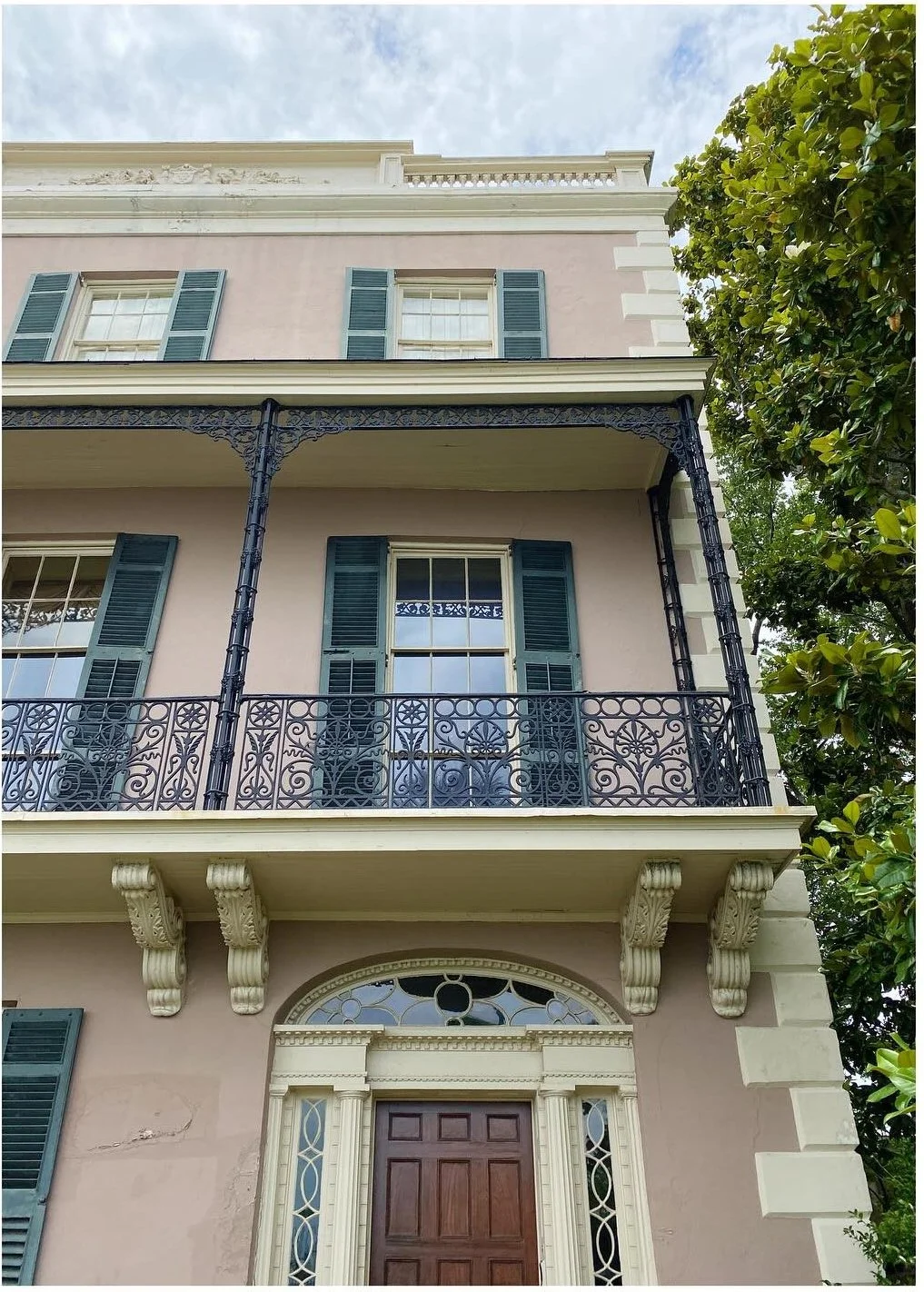 Pale historic house with dark iron balcony and green shutters
