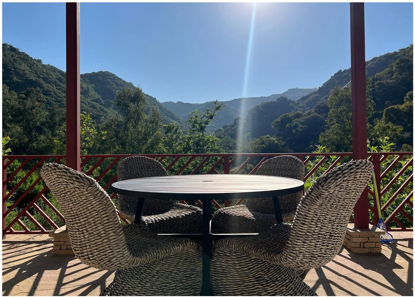 Round outdoor dining table and woven chairs overlooking wooded hills
