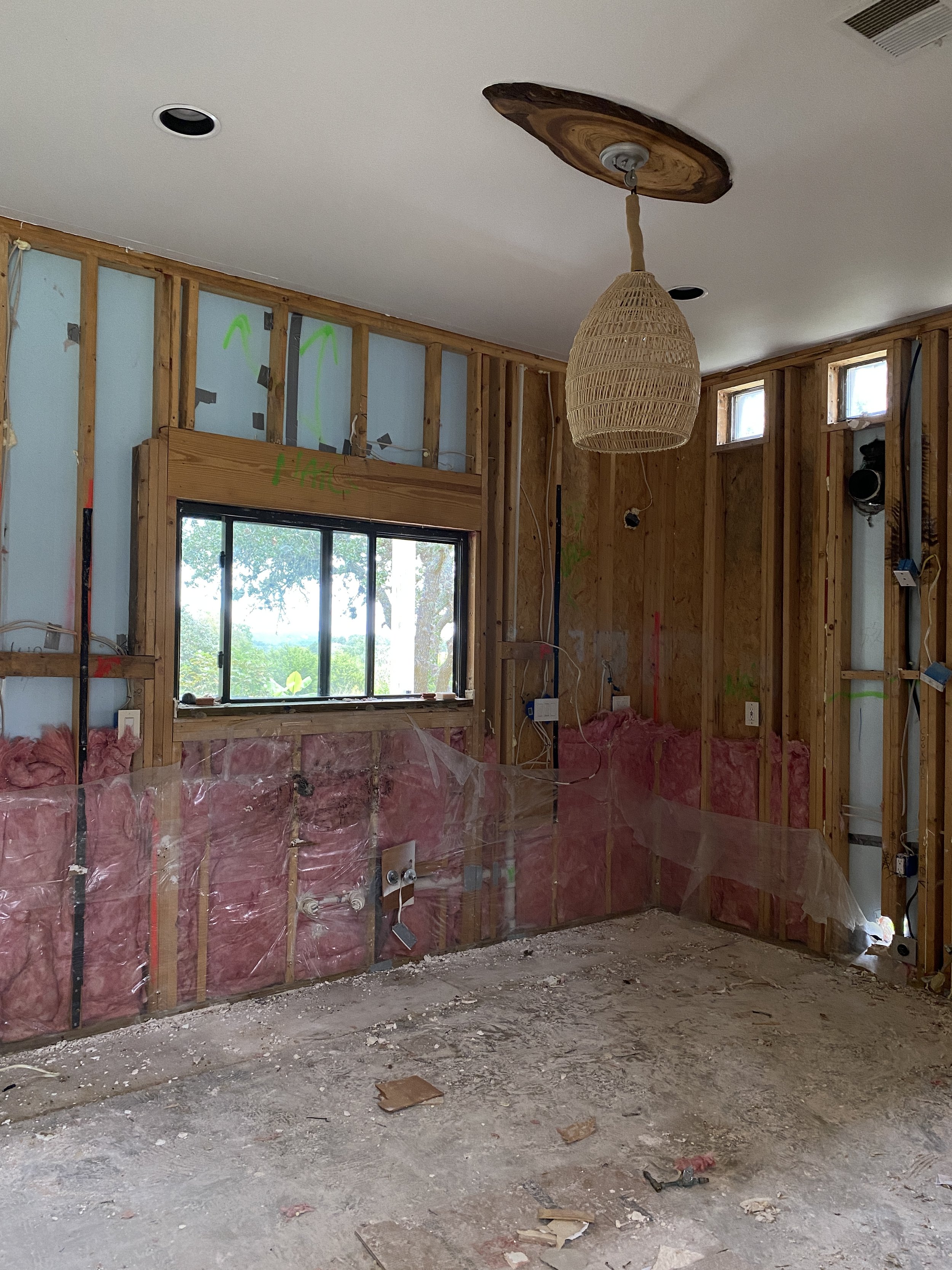Room under renovation with exposed framing, insulation, and a hanging light.