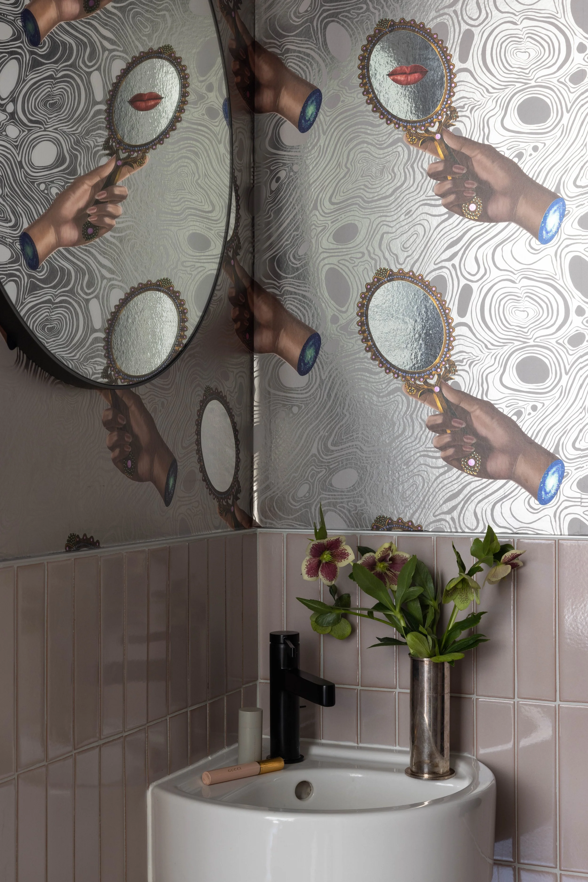 Bathroom with patterned wallpaper, a rounded mirror, and dark wall faucets.