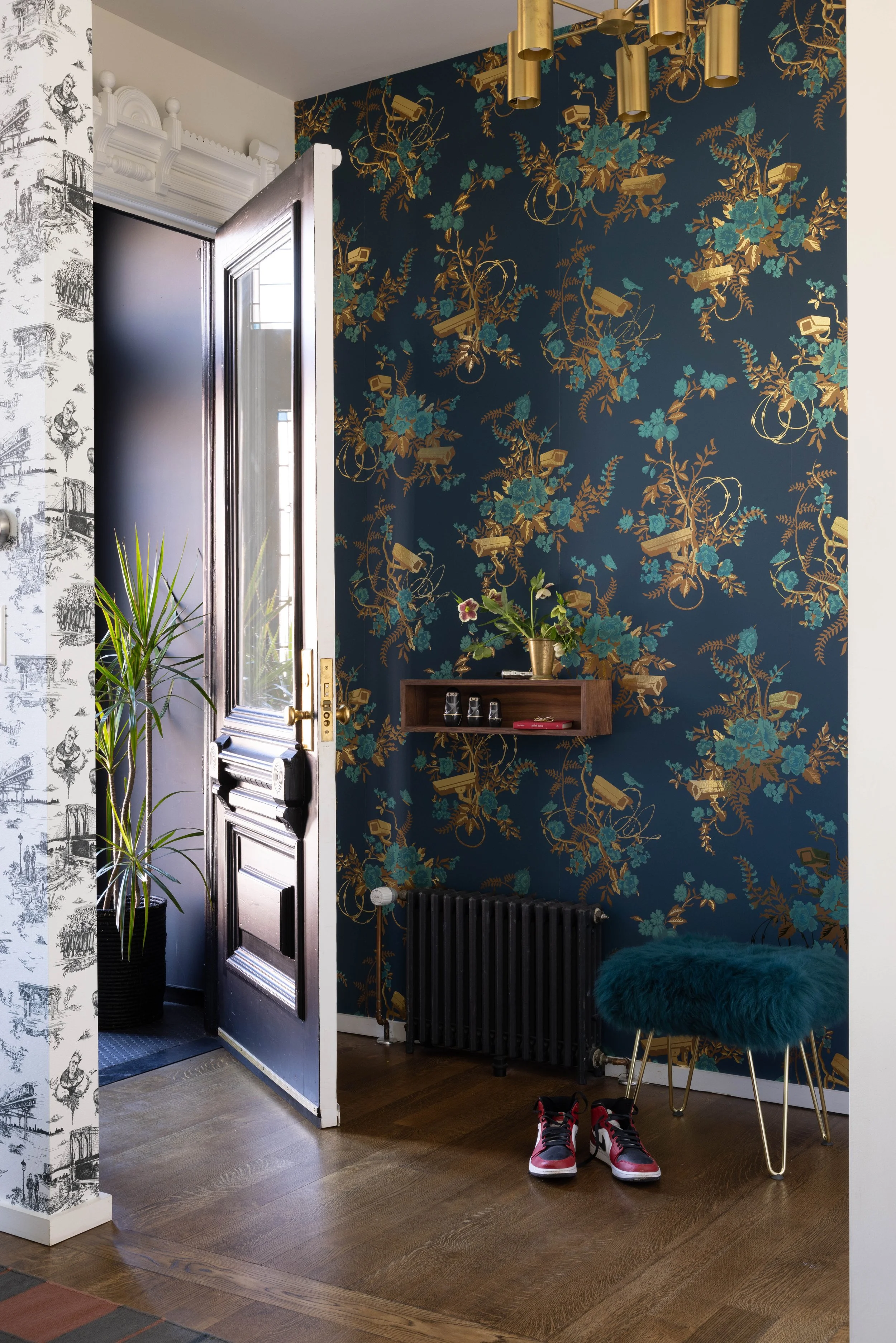 Hallway with dark floral wallpaper, contrasting white patterned wall, black radiator, and wood flooring.