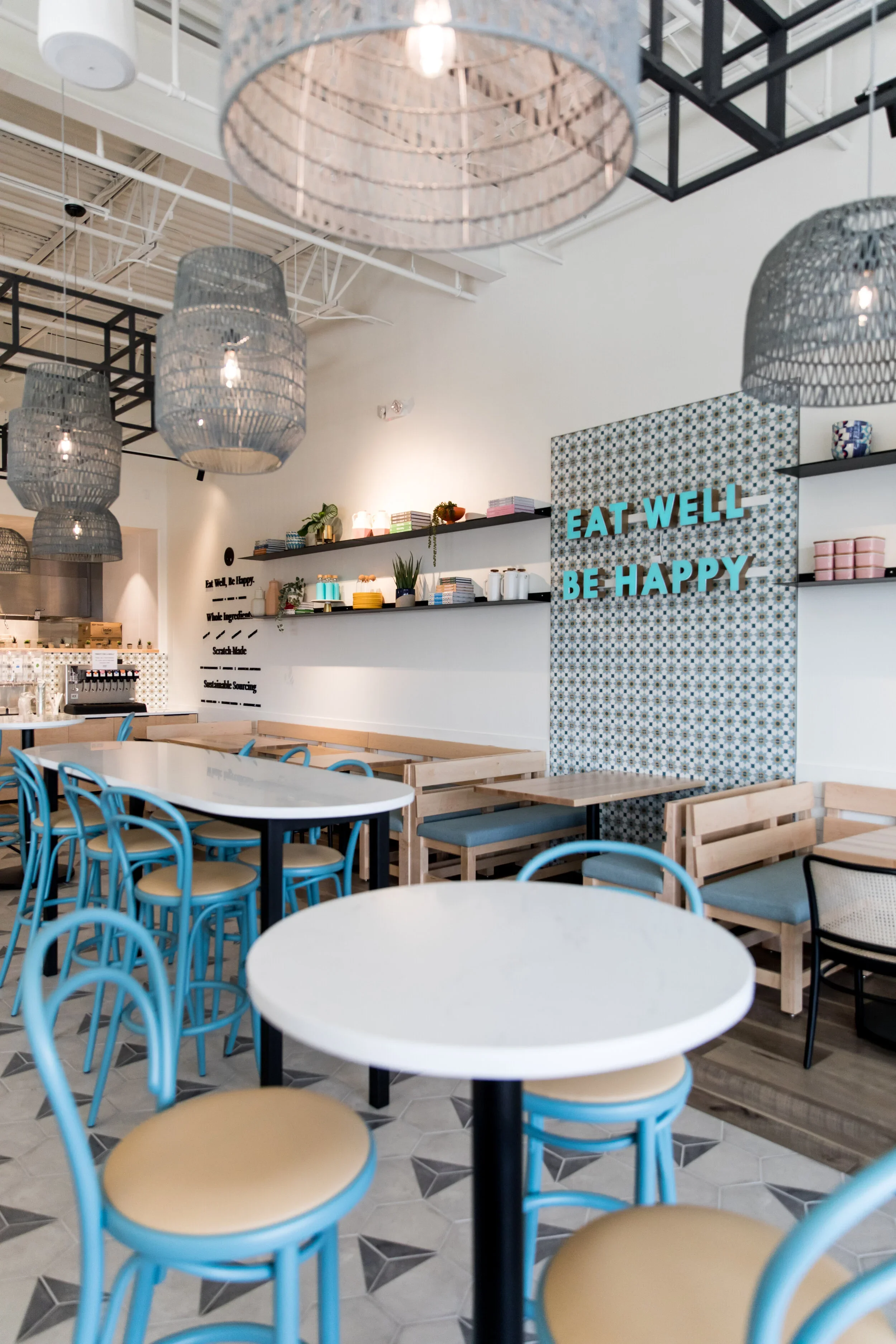 Restaurant seating with blue bentwood chairs, white round tables, wood banquettes, gray woven pendants, and patterned feature wall. Photography by Nathan Warmes