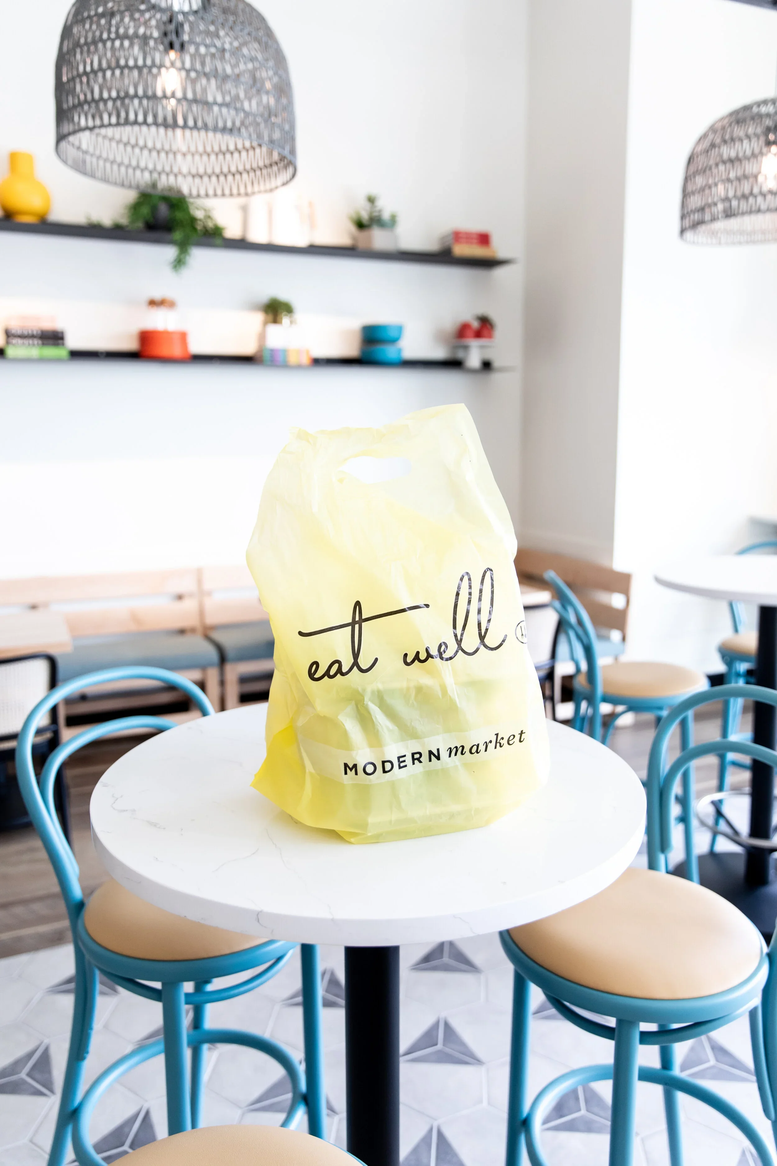 Restaurant table with yellow display, blue bentwood chairs, wood banquette, and shelves of colorful ceramics and plants. Photography by Nathan Warmes