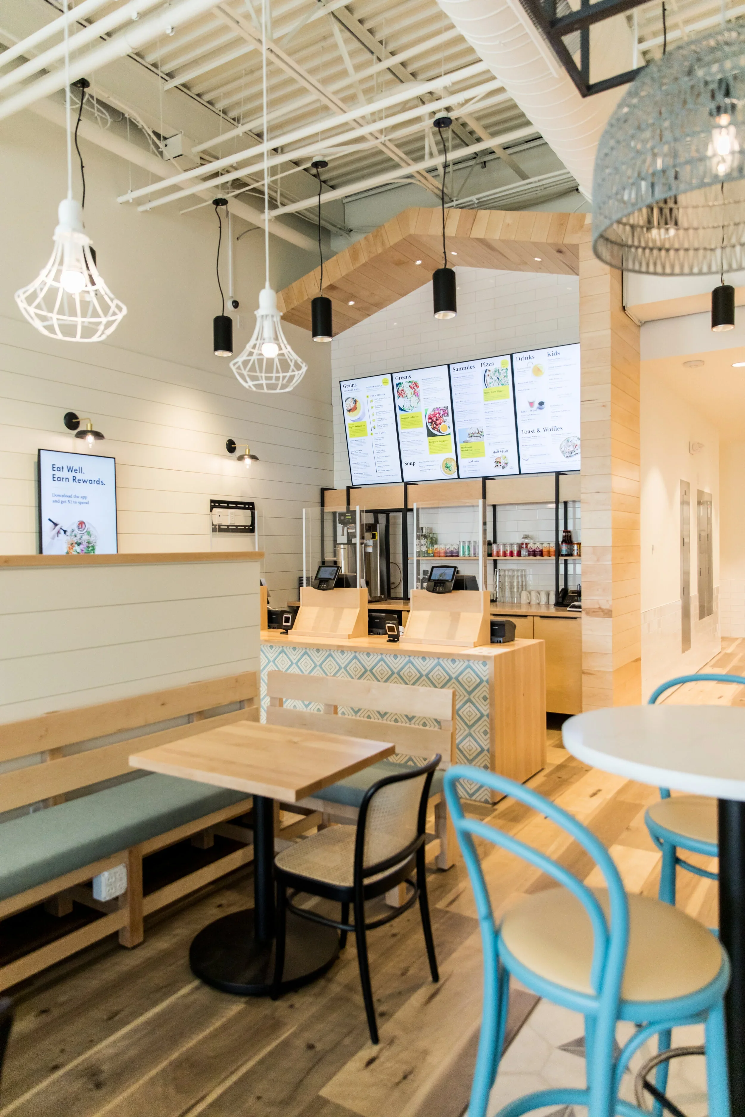 Restaurant interior with communal wood table, mixed chairs, white cage pendants, wood-framed counter, and framed artwork. Photography by Nathan Warmes