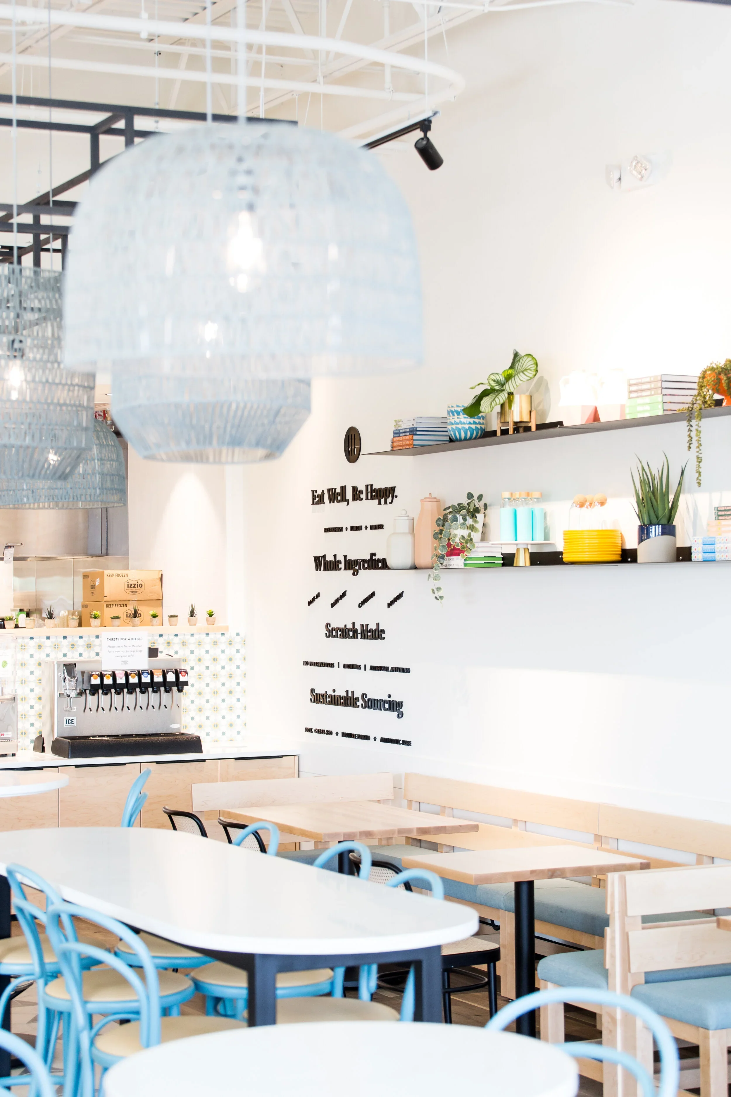 Restaurant dining corner with white shiplap walls, floating shelves, gray pendant shades, pale wood tables, and banquettes. Photography by Nathan Warmes