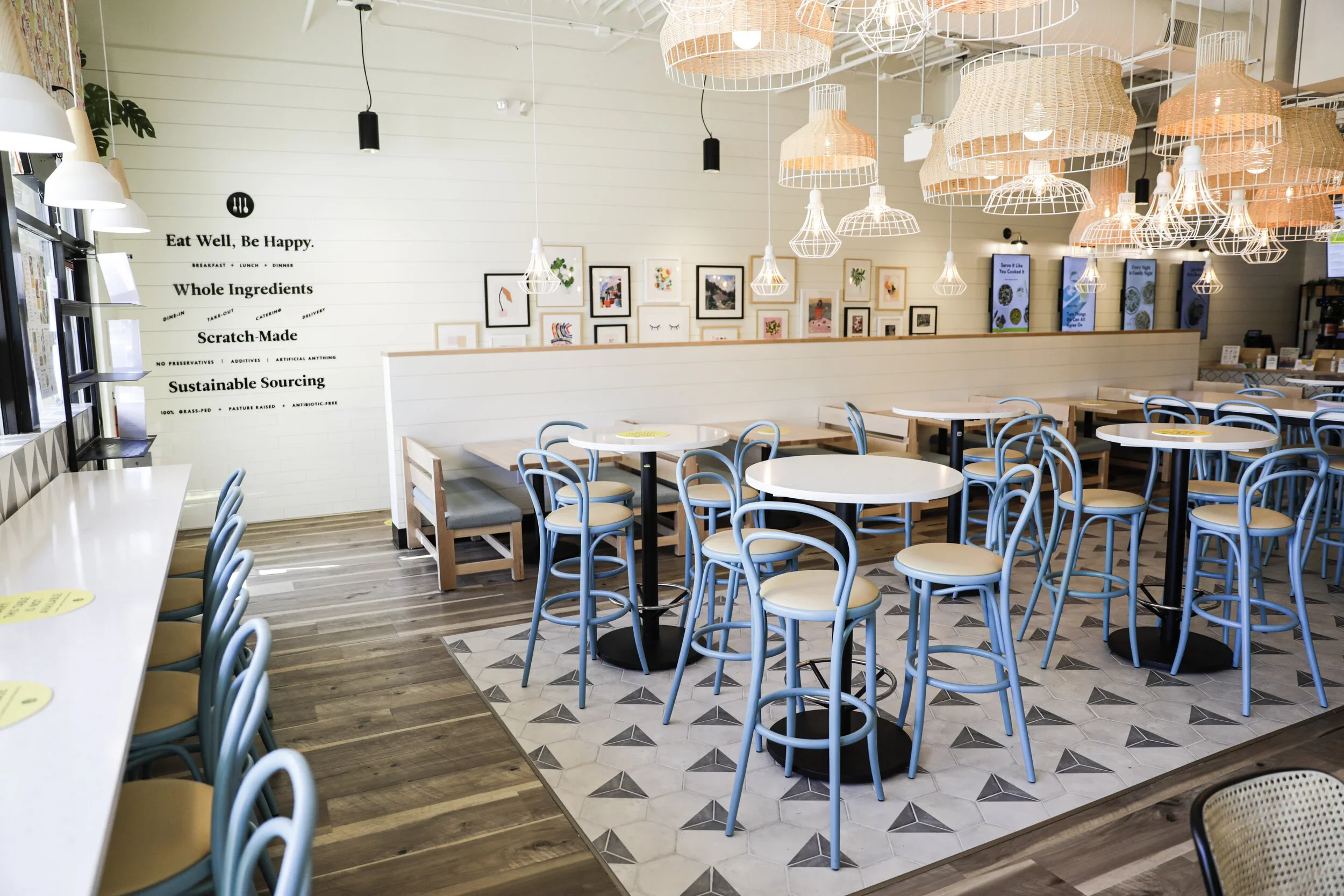 Restaurant dining room with blue bentwood chairs, pale tables, wood banquettes, triangular floor tile, and mixed pendant lights. Photography by Nathan Warmes
