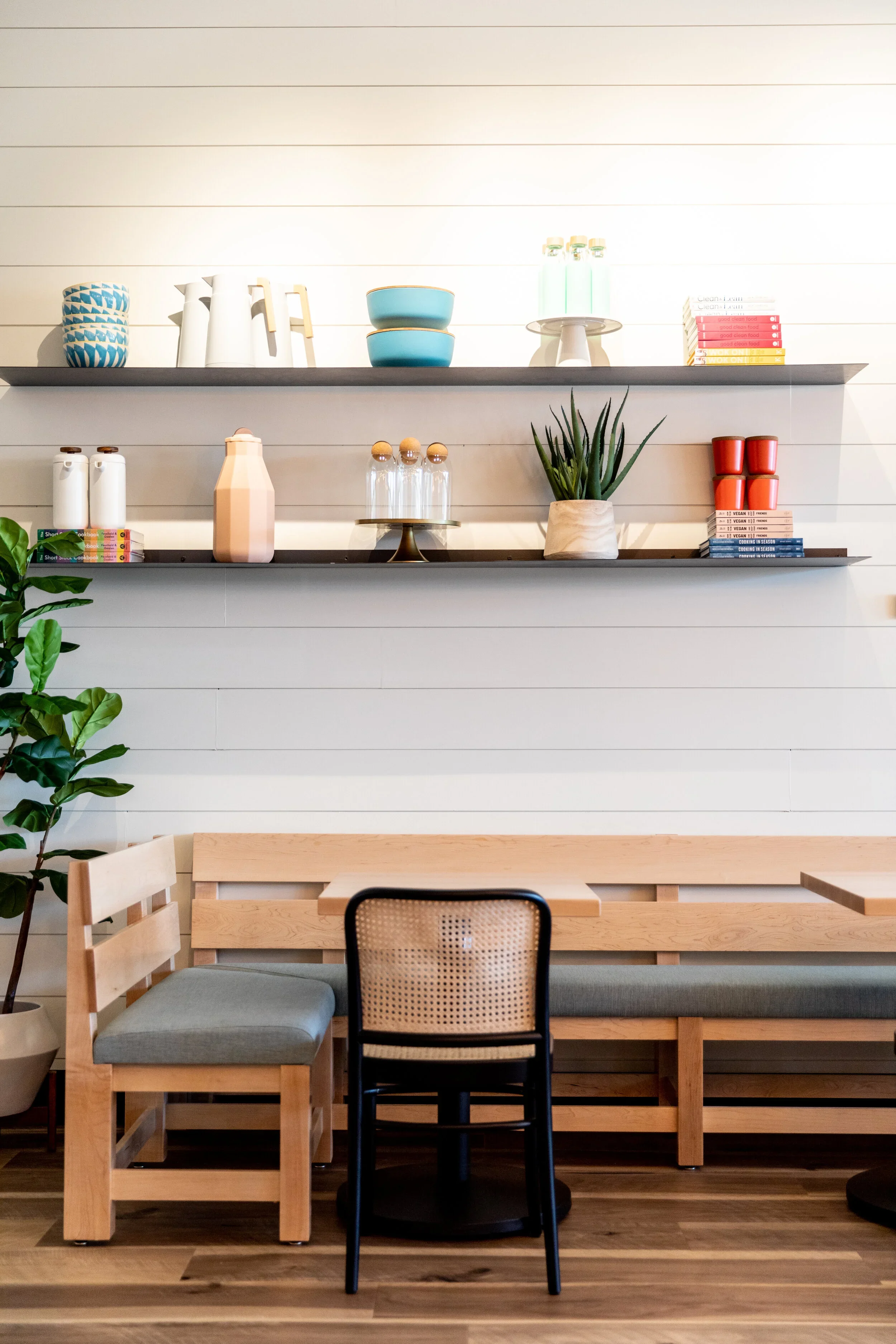 Restaurant banquette with wood slat back, gray cushions, black cane-back chair, floating shelves, and white shiplap walls. Photography by Nathan Warmes