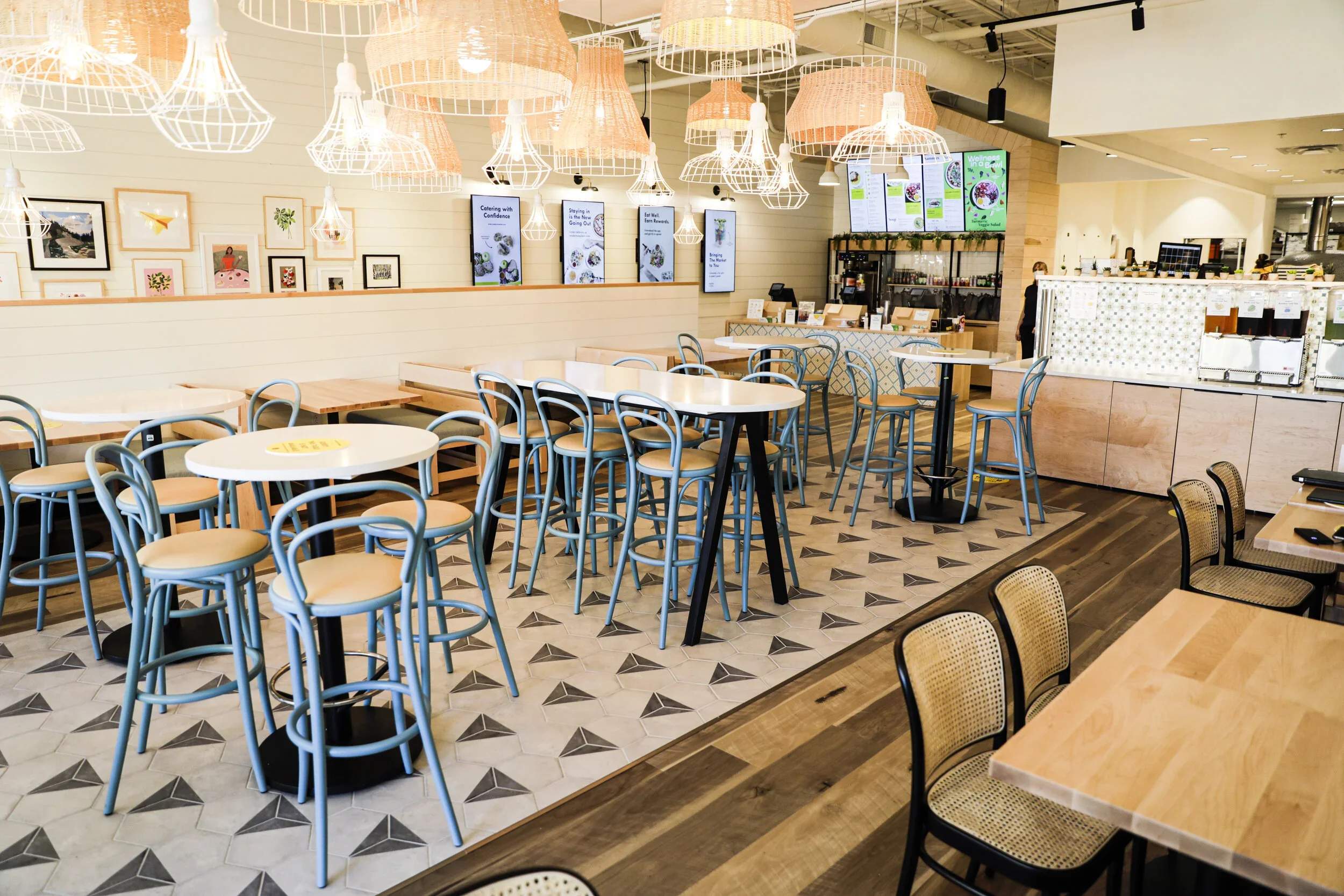 Restaurant dining area with blue chairs, round tables, wood banquettes, triangular floor tile, and clustered sculptural pendants. Photography by Nathan Warmes