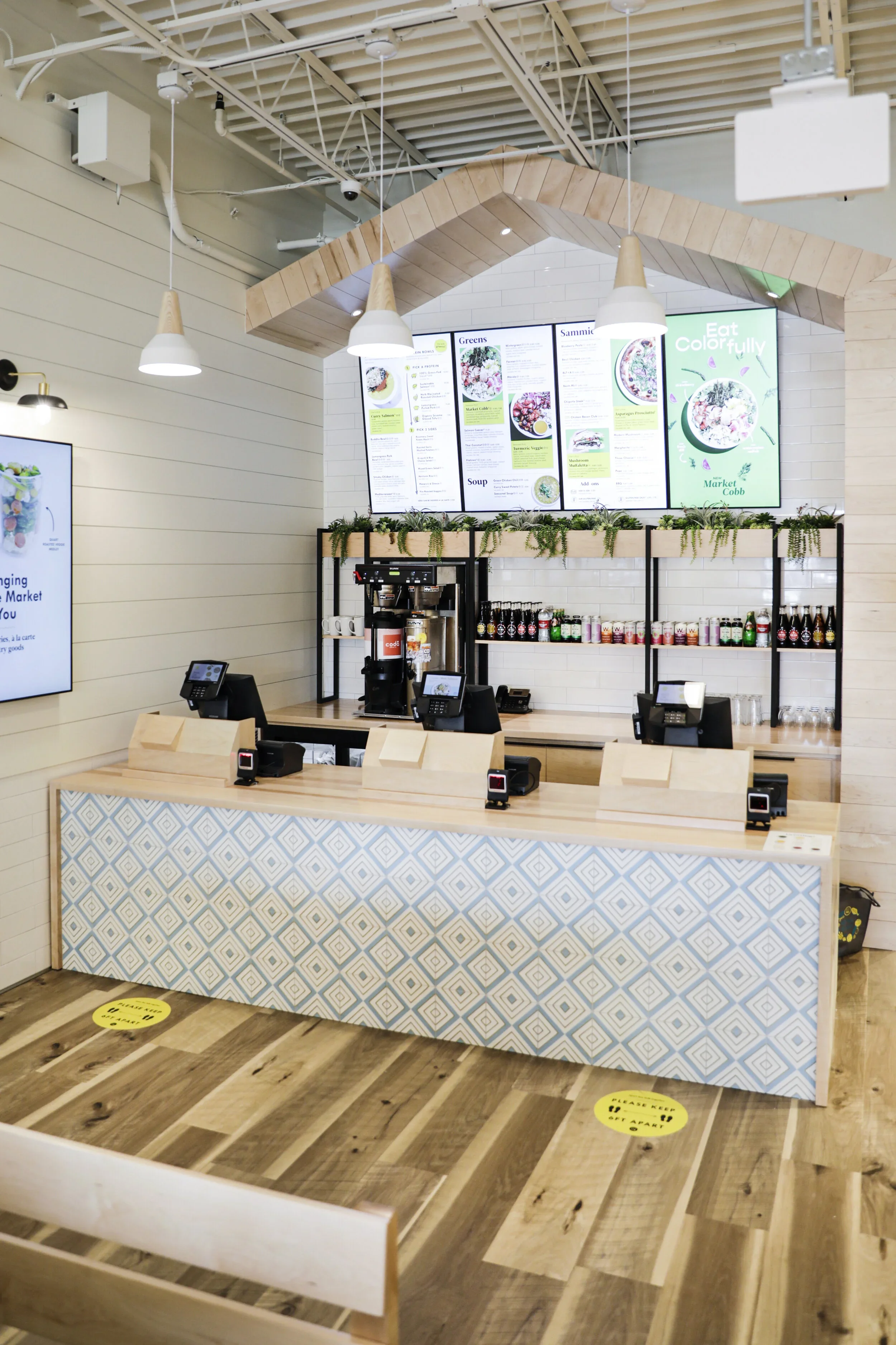 Restaurant counter with blue diamond-patterned tile, pale wood top, black shelving, digital menus, and angular wood canopy. Photography by Nathan Warmes
