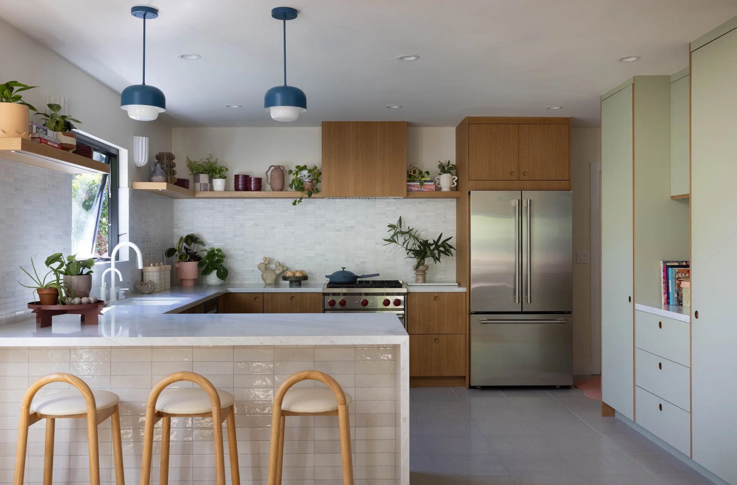  Crimson and Clover ↗  Sage cabinetry, an oak island, and blue pendant lights.