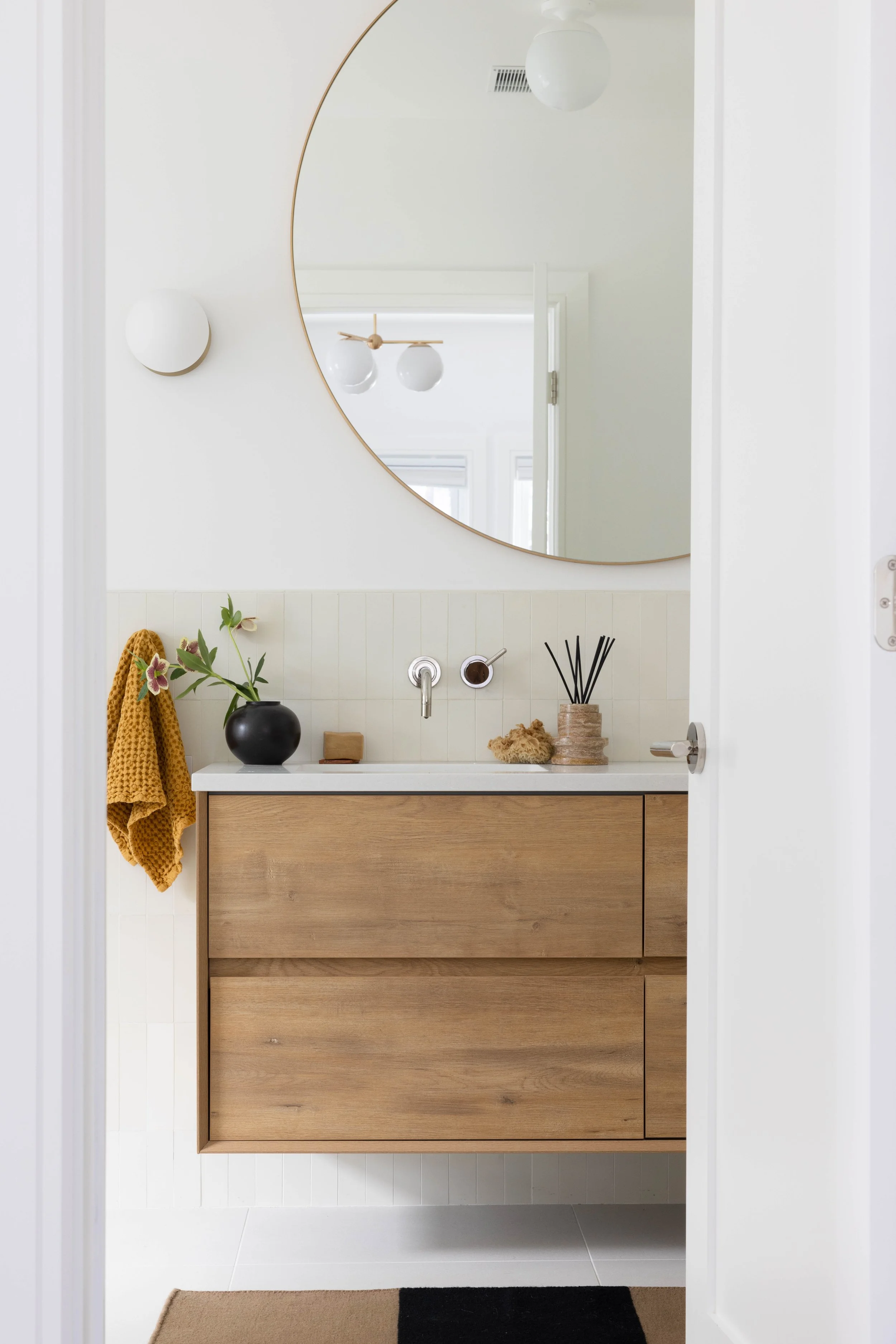 Bathroom with a pale wood vanity beneath a large round mirror.