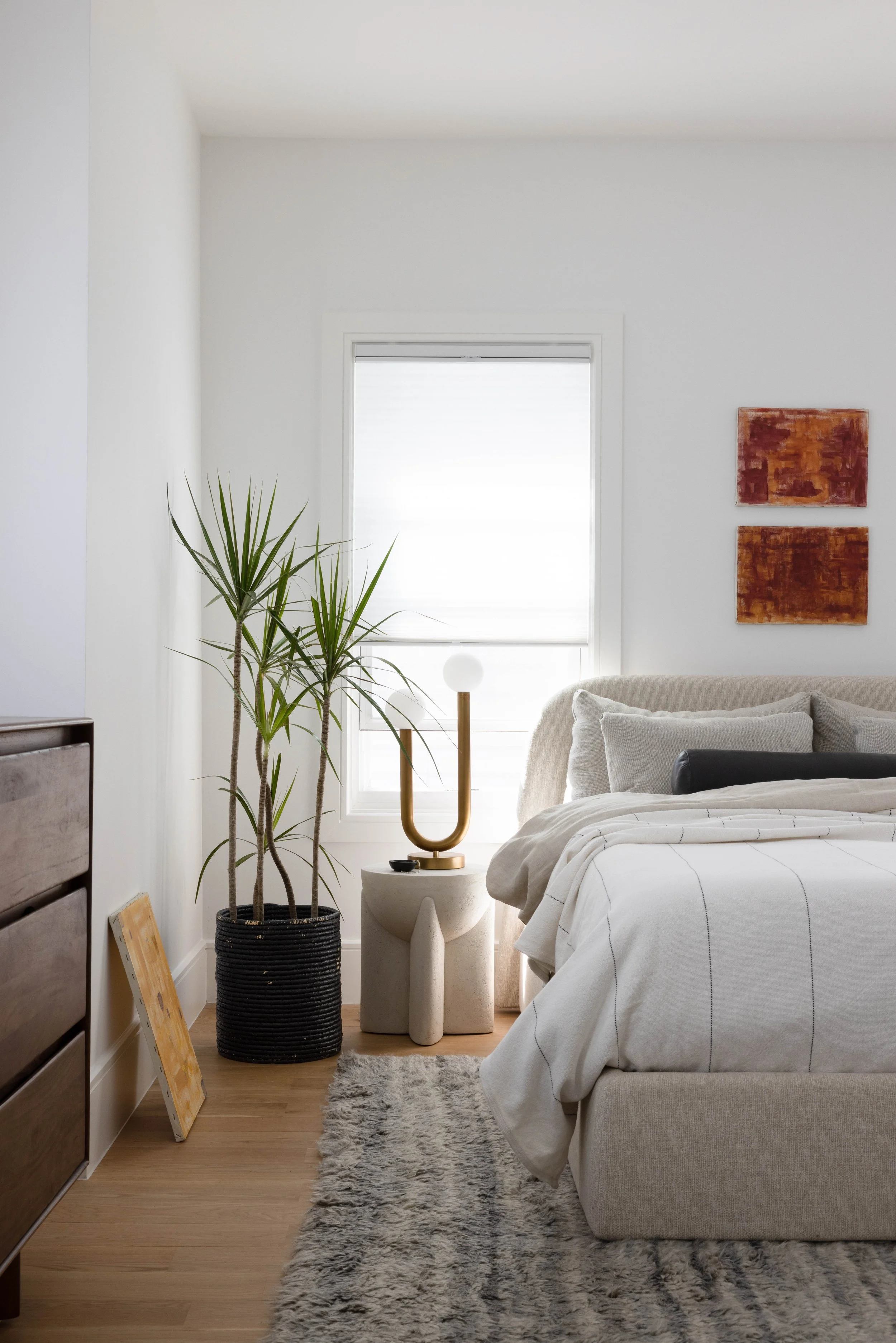Bedroom with a gray upholstered bed and a tall leafy plant.