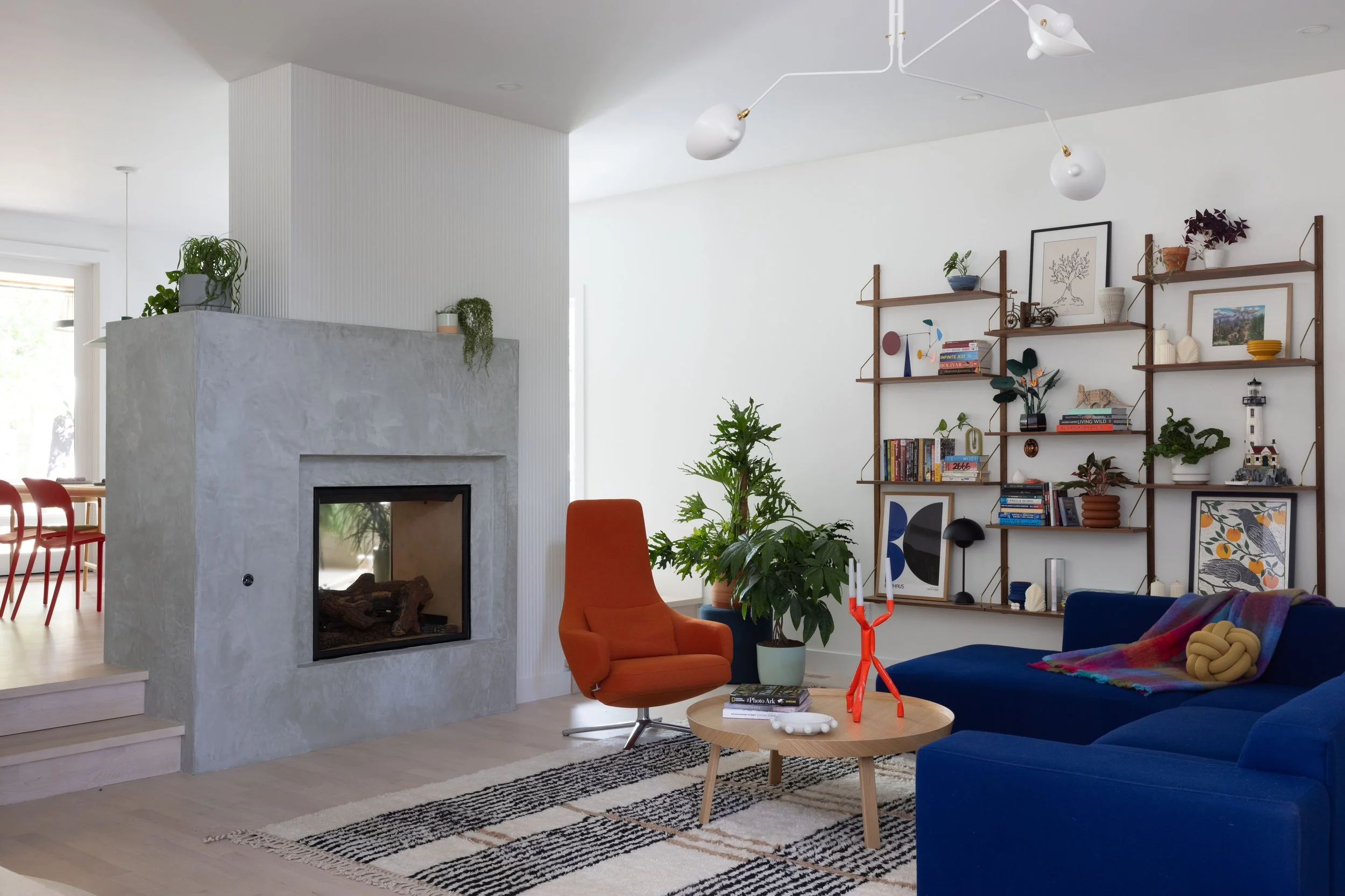 Living room with a concrete fireplace, blue sofa, and orange chair.
