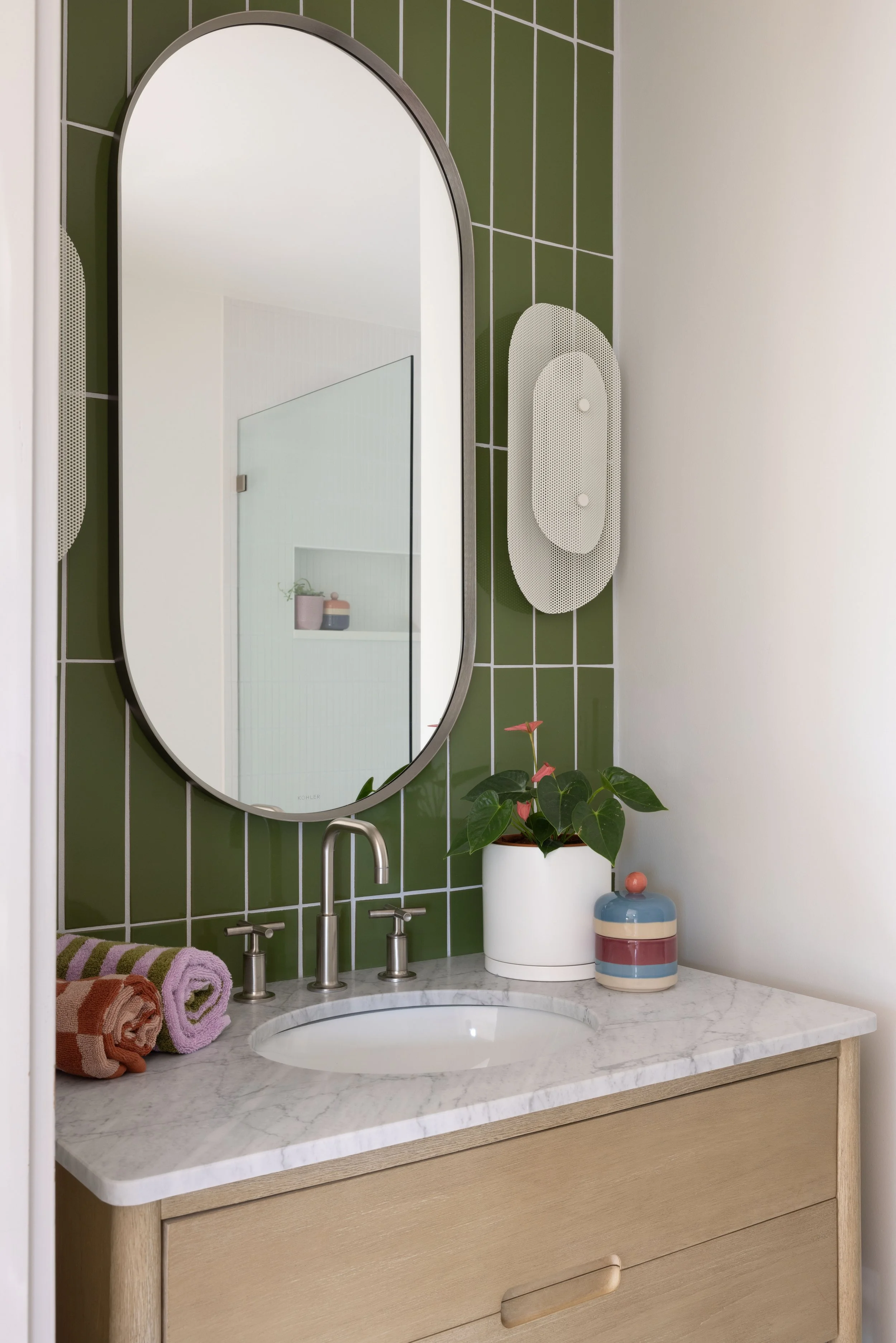 Bathroom vanity with green tile and shaped mirrors.