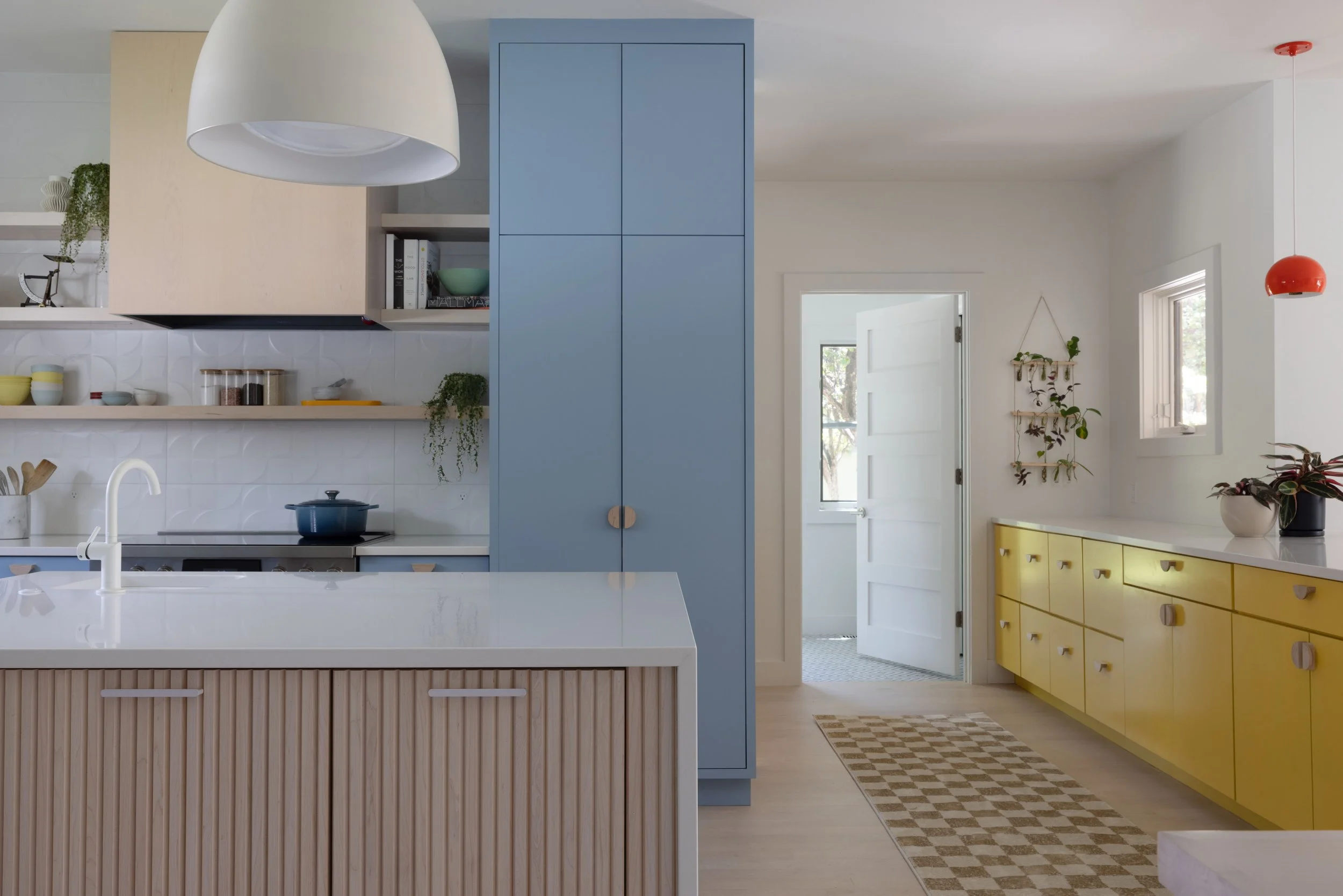 Kitchen with yellow cabinets, blue pantry storage, and a fluted island.