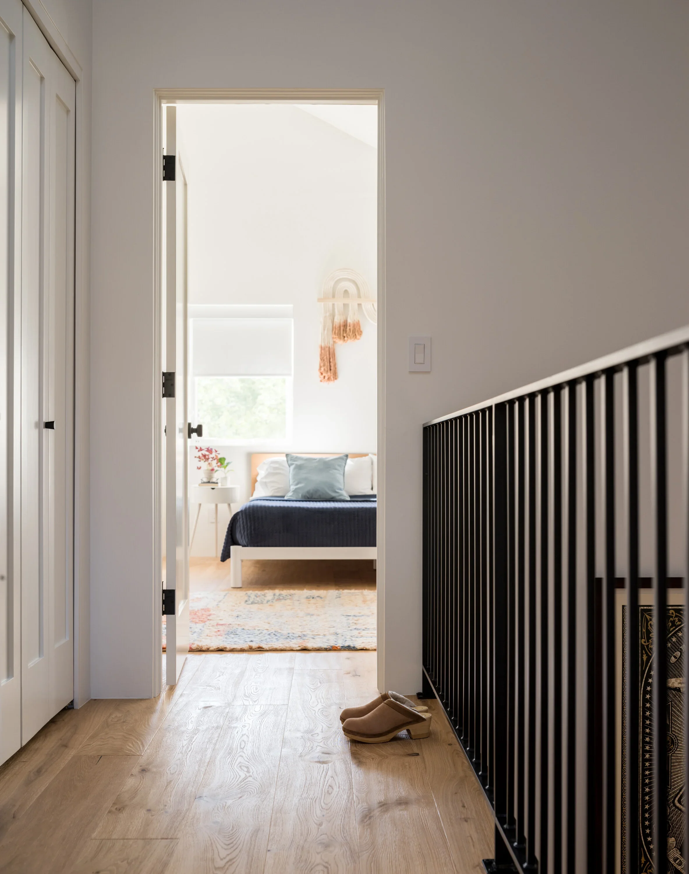 Hallway with pale wood floors and black metal stair railings.