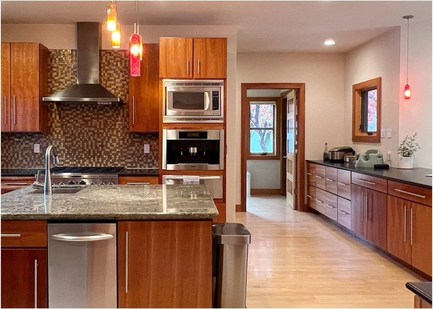 Original kitchen with warm wood cabinets dark counters and red pendants