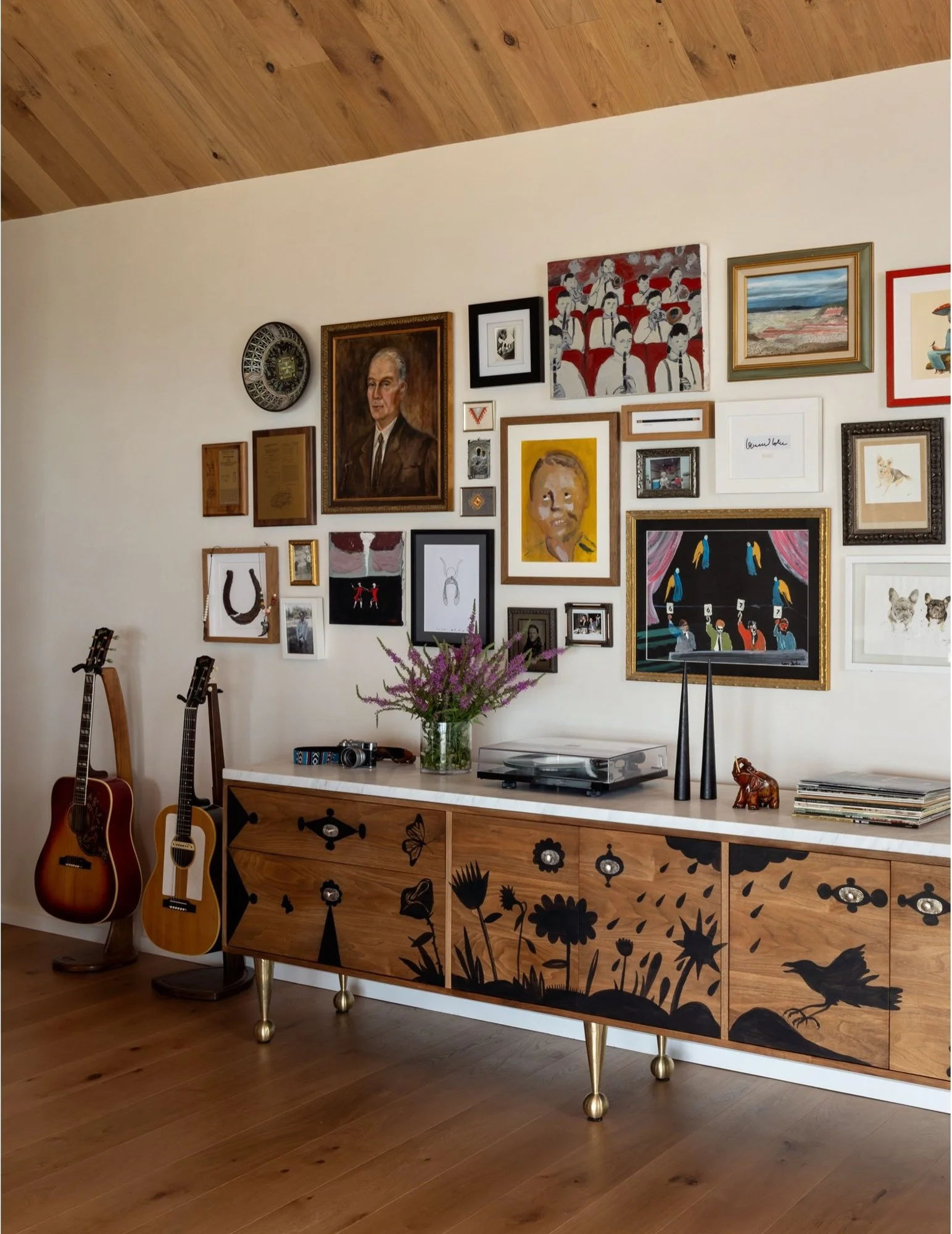 Sculpted wood sideboard below a gallery wall of framed art
