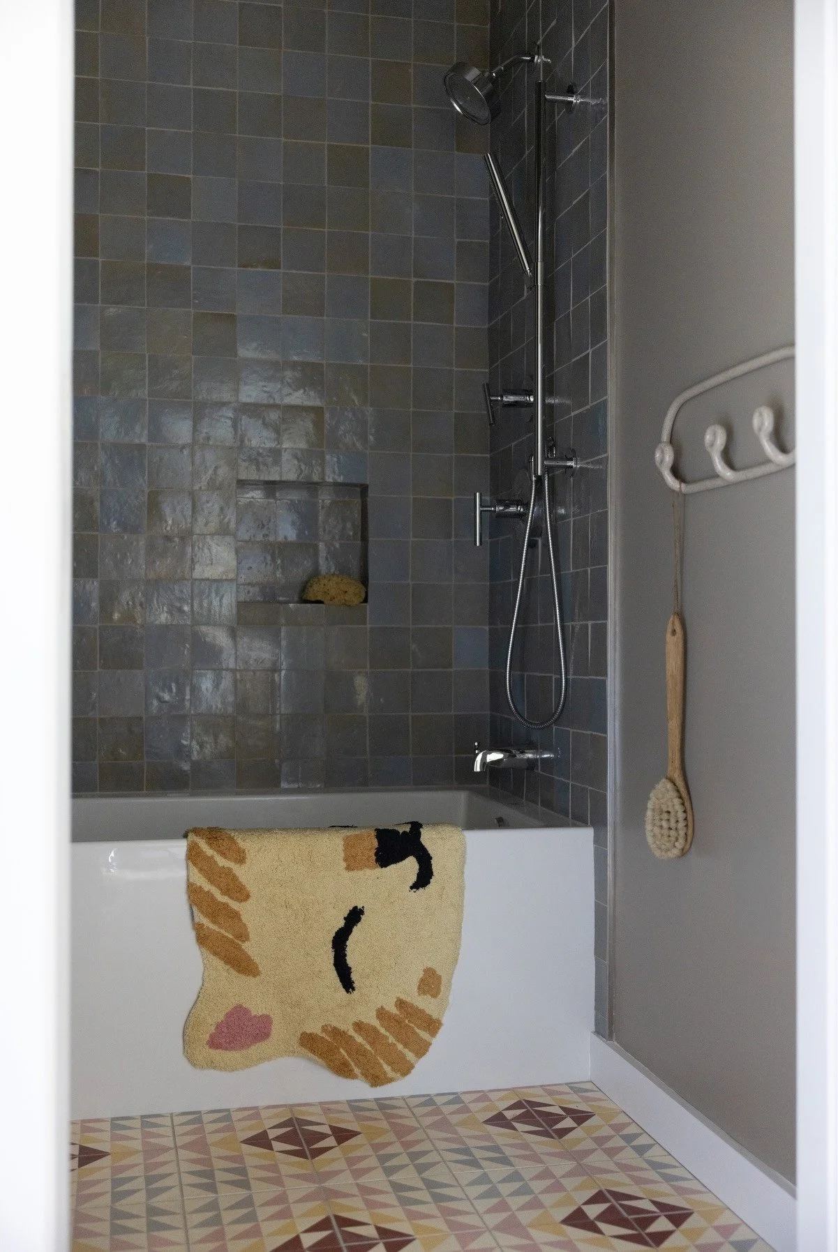 Blue tiled shower with a patterned curtain and brass controls