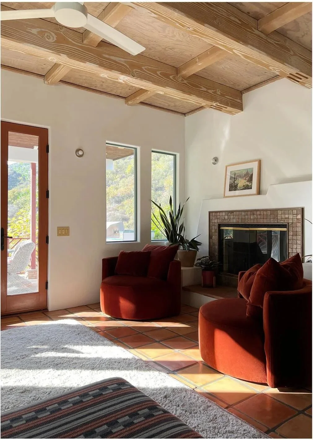 Rust-colored lounge chair beside a pale rug under exposed wood beams