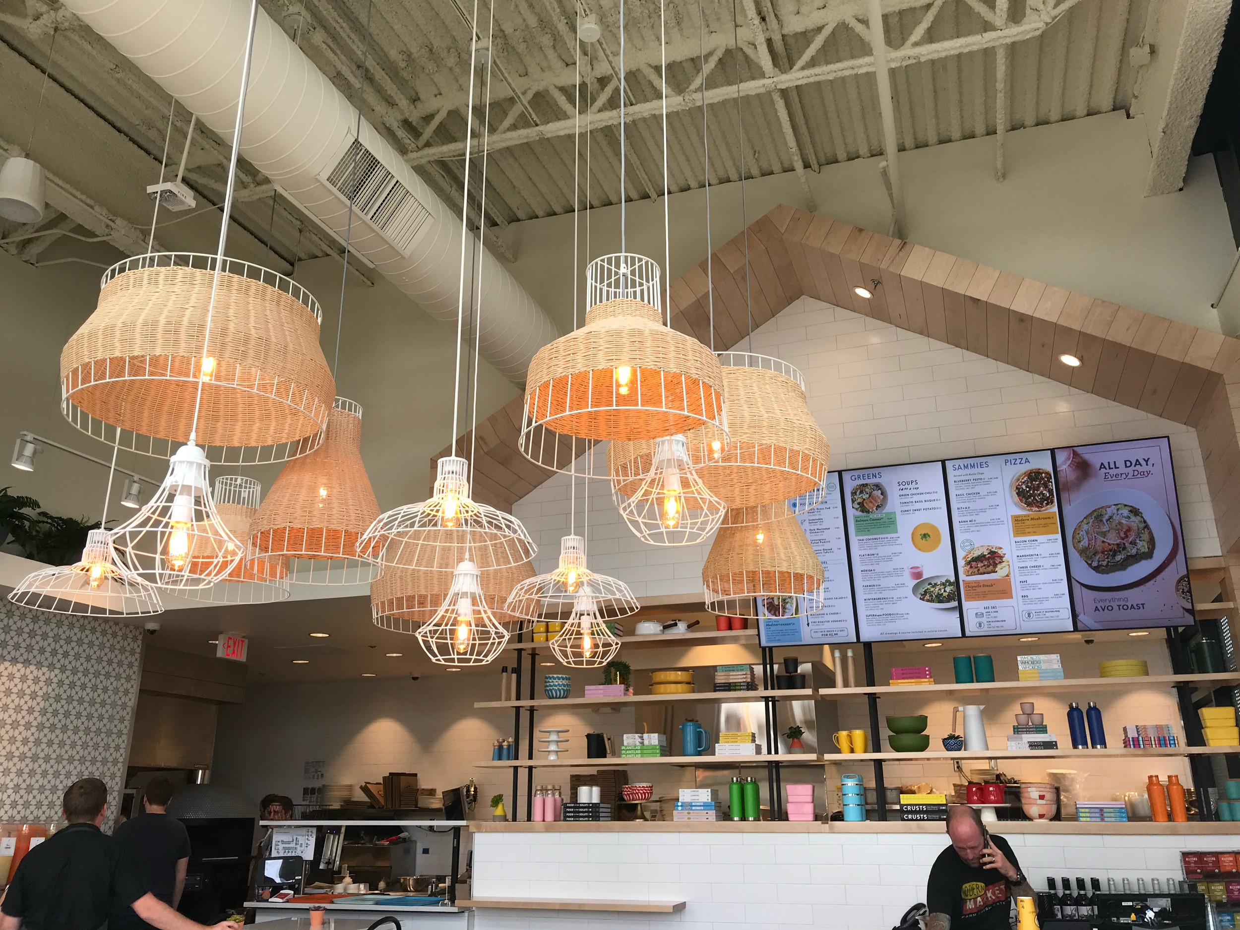 Restaurant counter with woven pendant lights, open shelving, and menu boards.