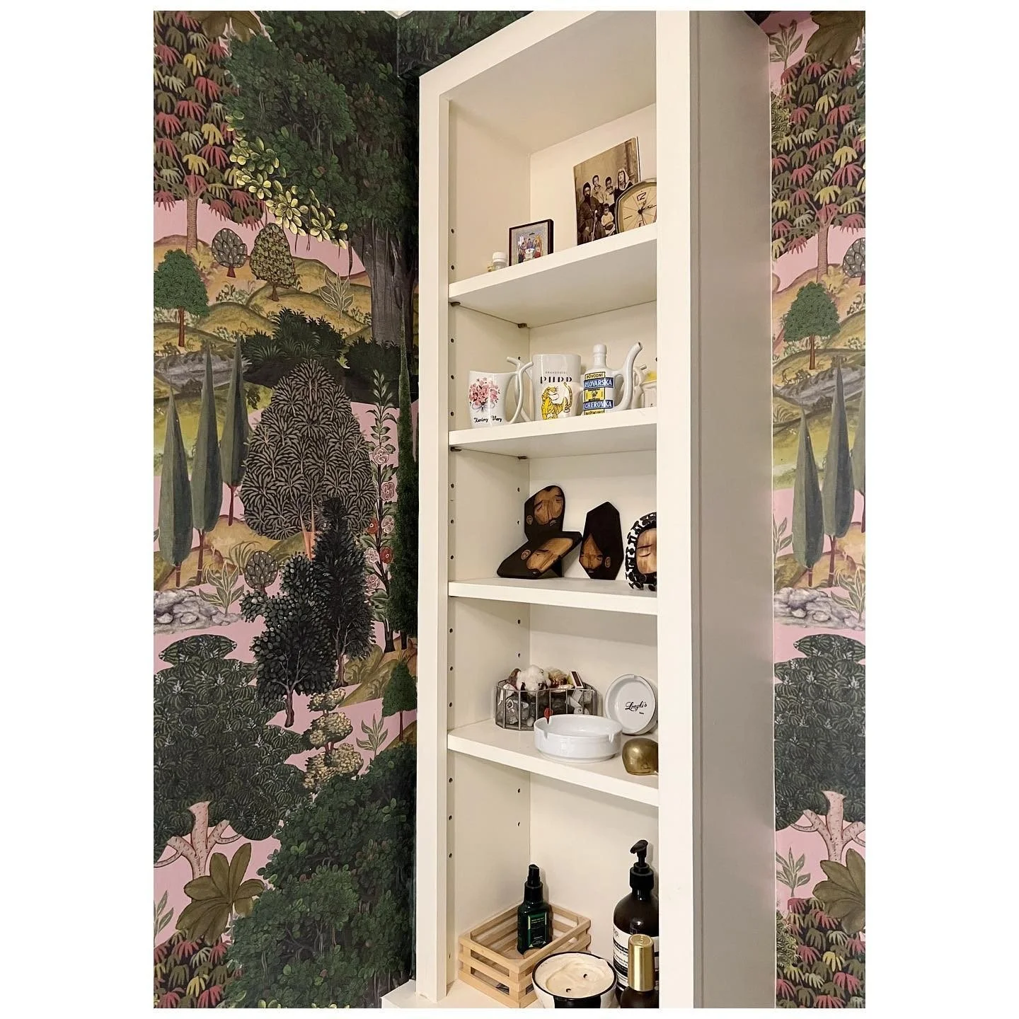 White recessed shelves against lush landscape-patterned wallpaper