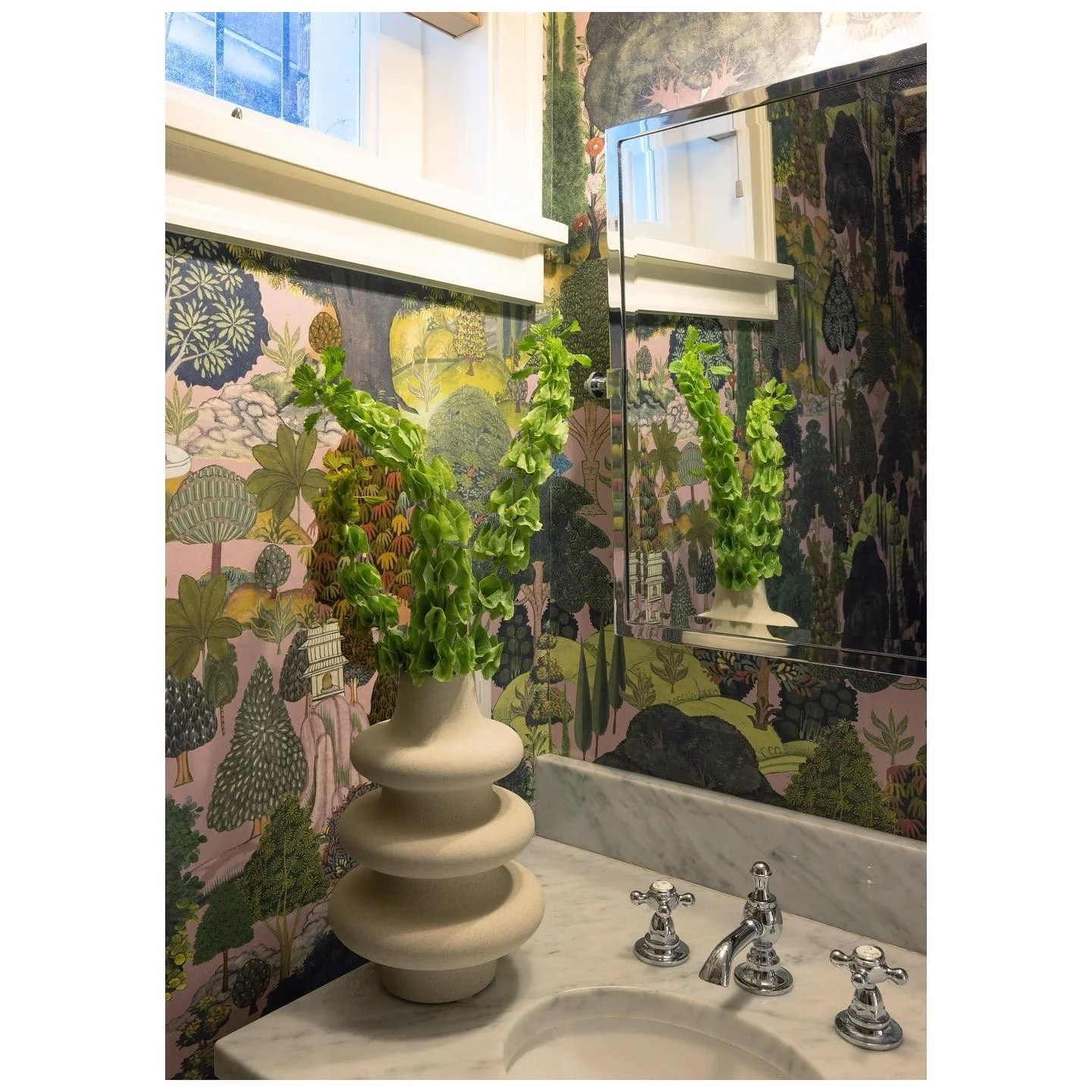 Sculptural pale vase beside a bathroom sink beneath botanical wallpaper