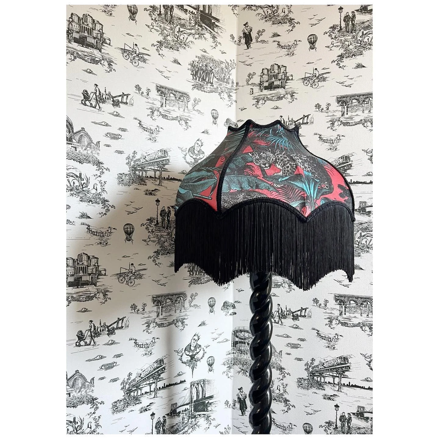 Decorative fringed lampshade against black-and-white illustrated toile wallpaper