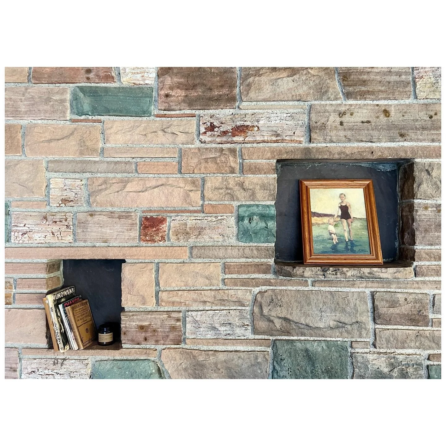 Small framed painting set into a rustic stone fireplace wall