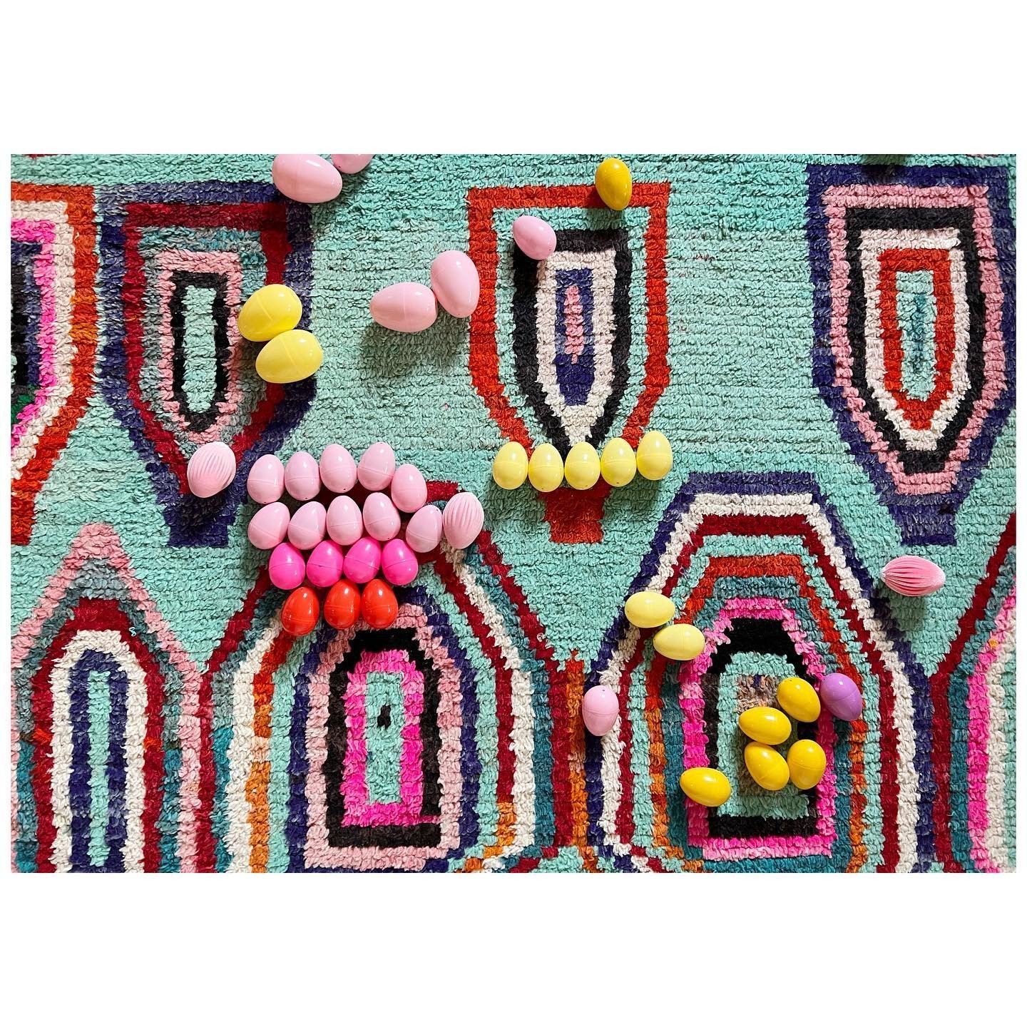 Vintage Moroccan rug with geometric colored lines beneath small pink and yellow objects