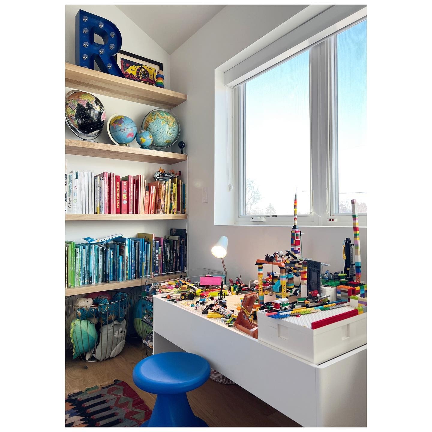 Books toys and display objects beside a white desk and sunlit bedroom window