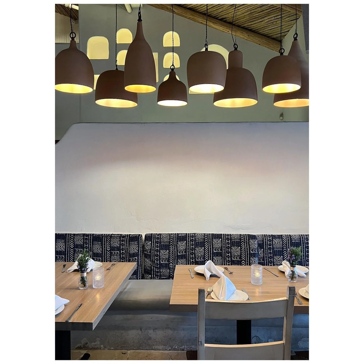 Restaurant dining tables beneath clusters of warm pendant lamps